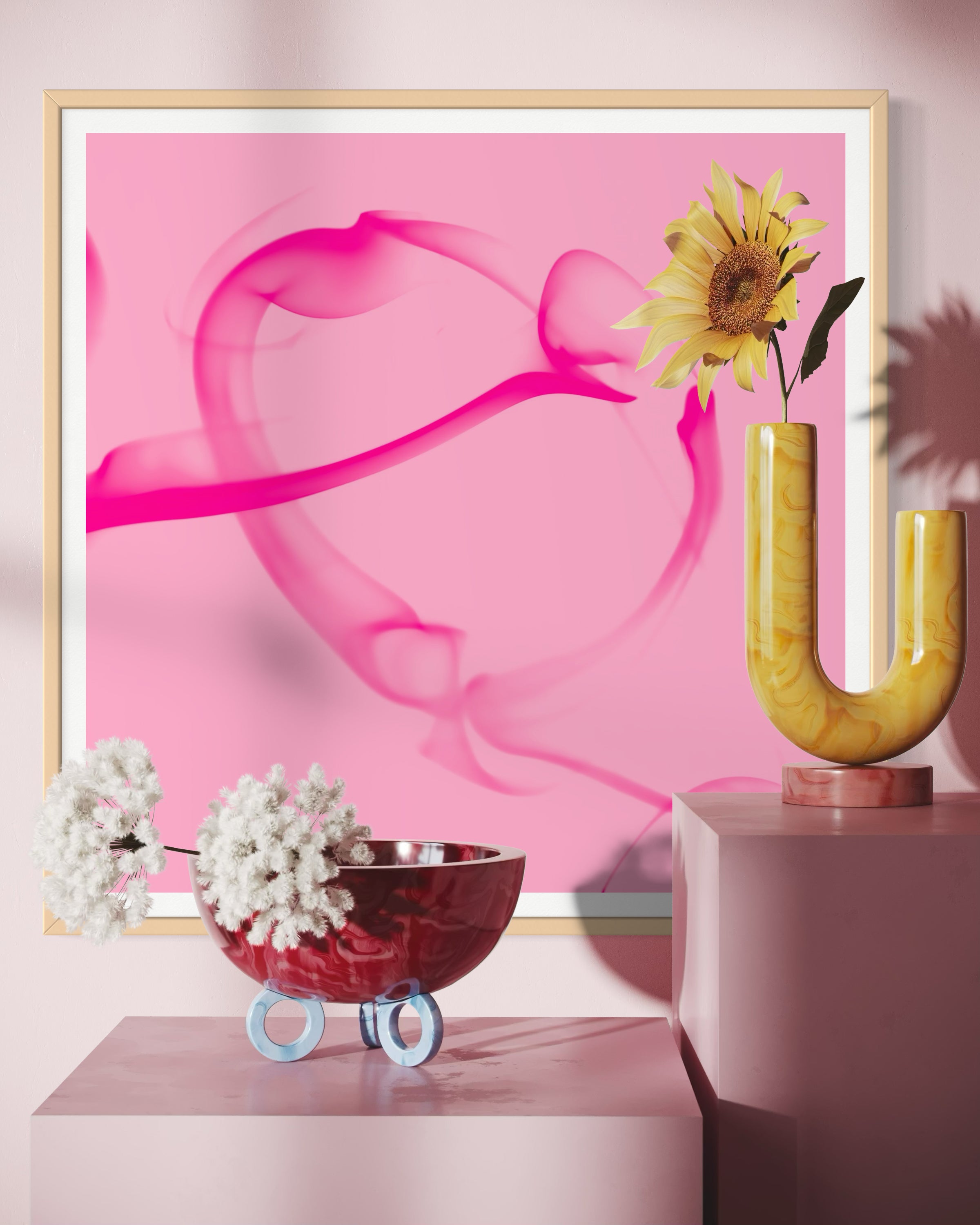 abstract pink heart on pink background in tan frame with white matte on wall behind a few flowers and above two light pink large cubes