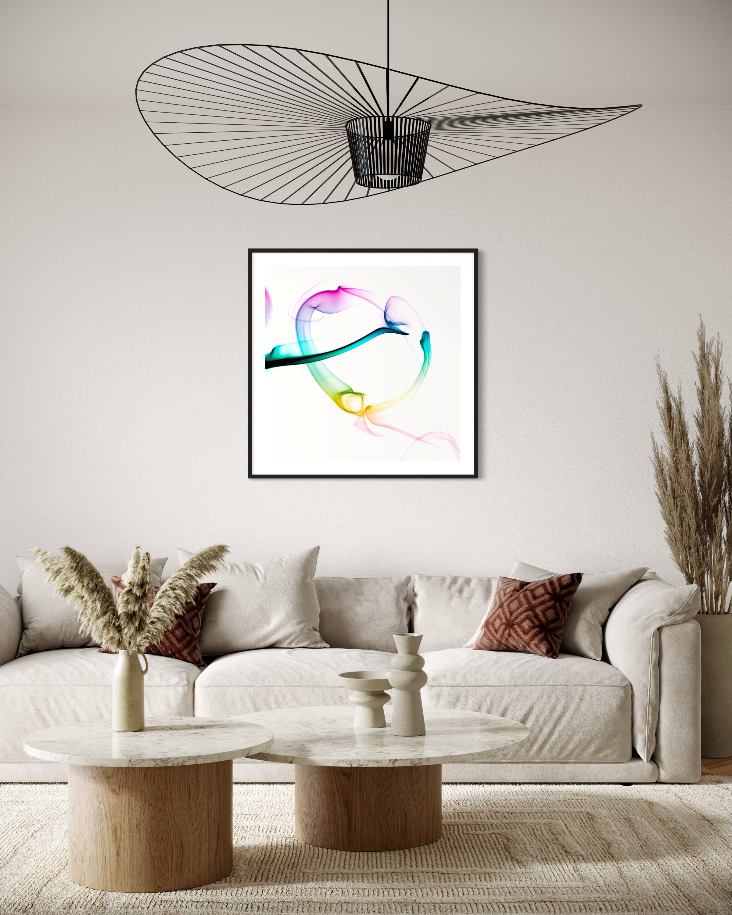 abstract heart in pink, green, gold, teal, red on white background in black frame with white matte on light gray wall above light tan sofa in earth toned living room