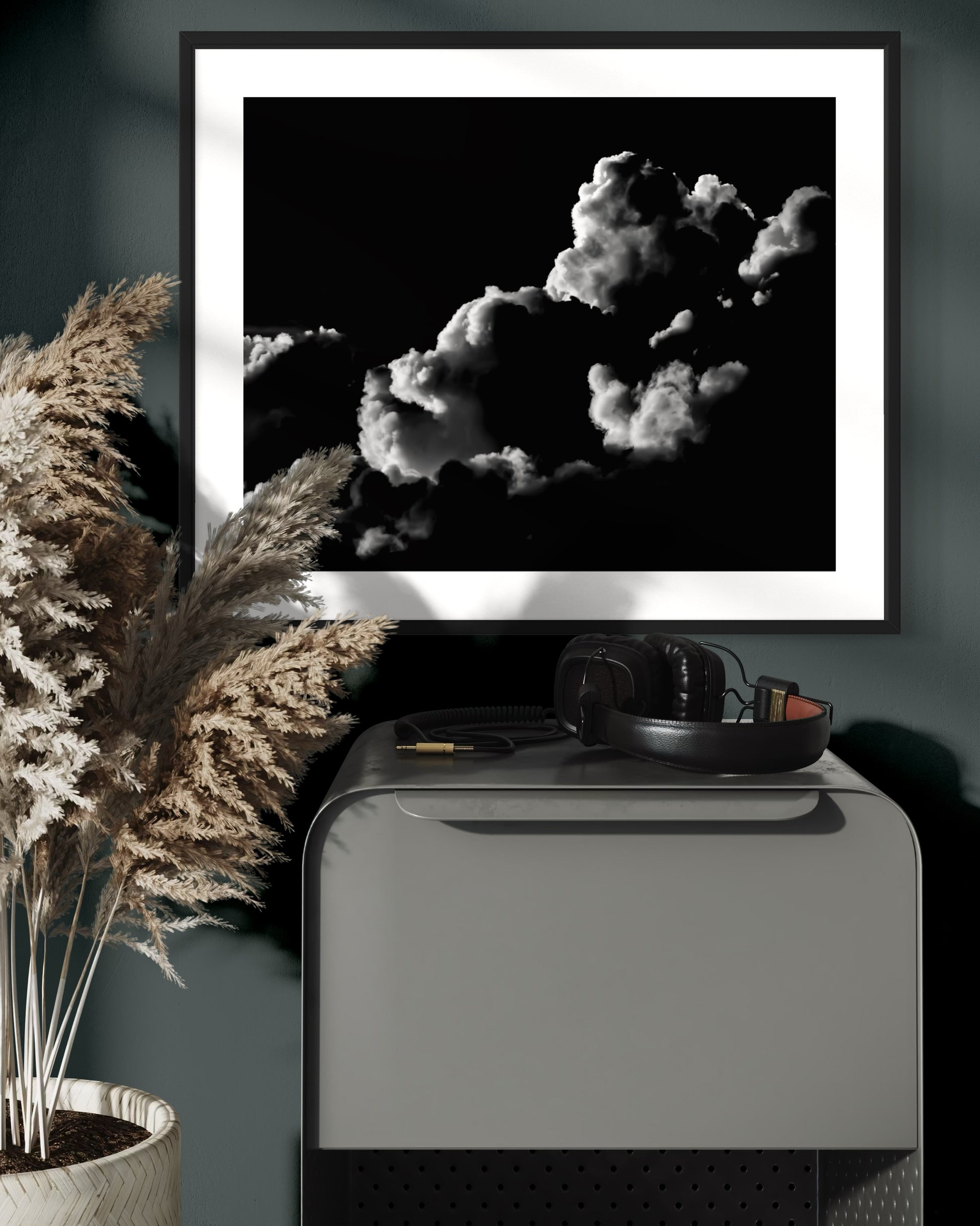 black and white photo of clouds, one looks like a dog's head in profile in black frame with white matte on cobalt colored wall above small piece of metal furniture with headphones on top