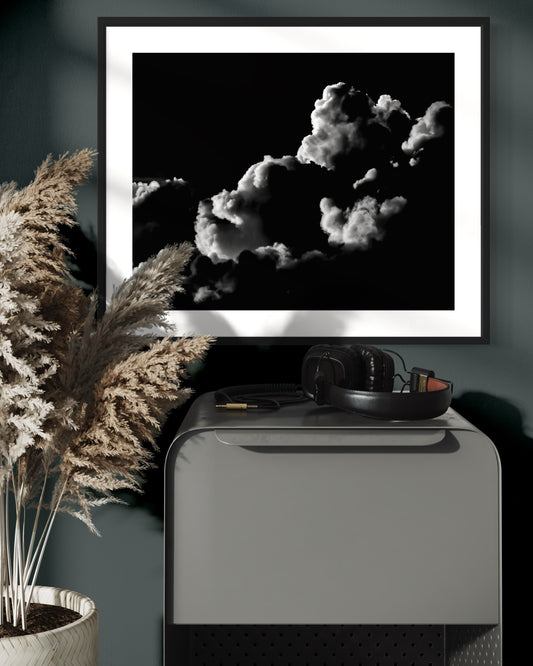 black and white photo of clouds, one looks like a dog's head in profile in black frame with white matte on cobalt colored wall above small piece of metal furniture with headphones on top