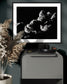 black and white photo of clouds, one looks like a dog's head in profile in black frame with white matte on cobalt colored wall above small piece of metal furniture with headphones on top