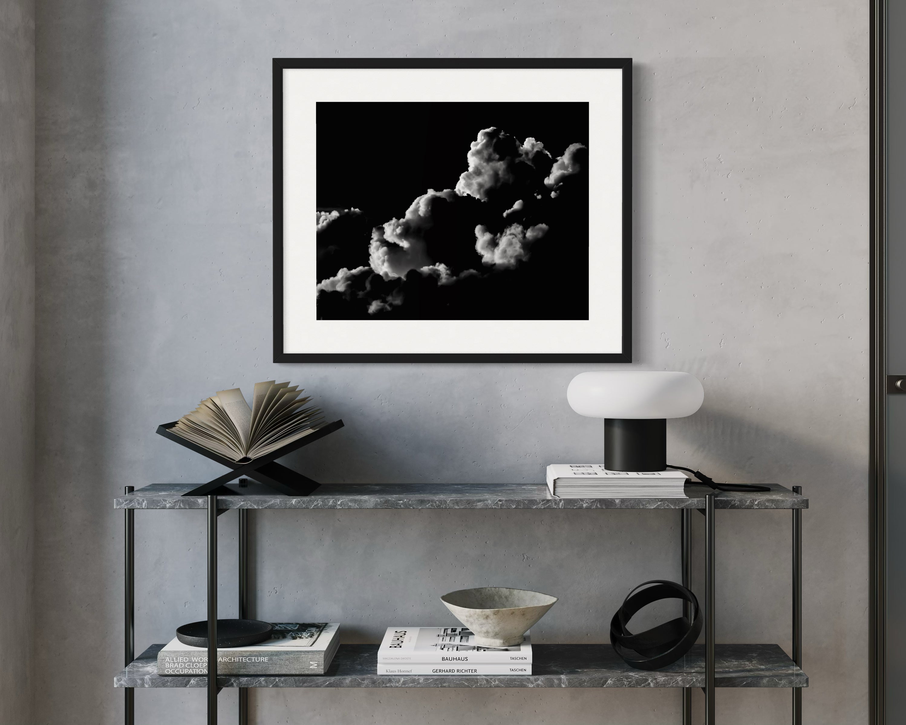 Framed black and white artwork on a wall above a shelf with decorative items.