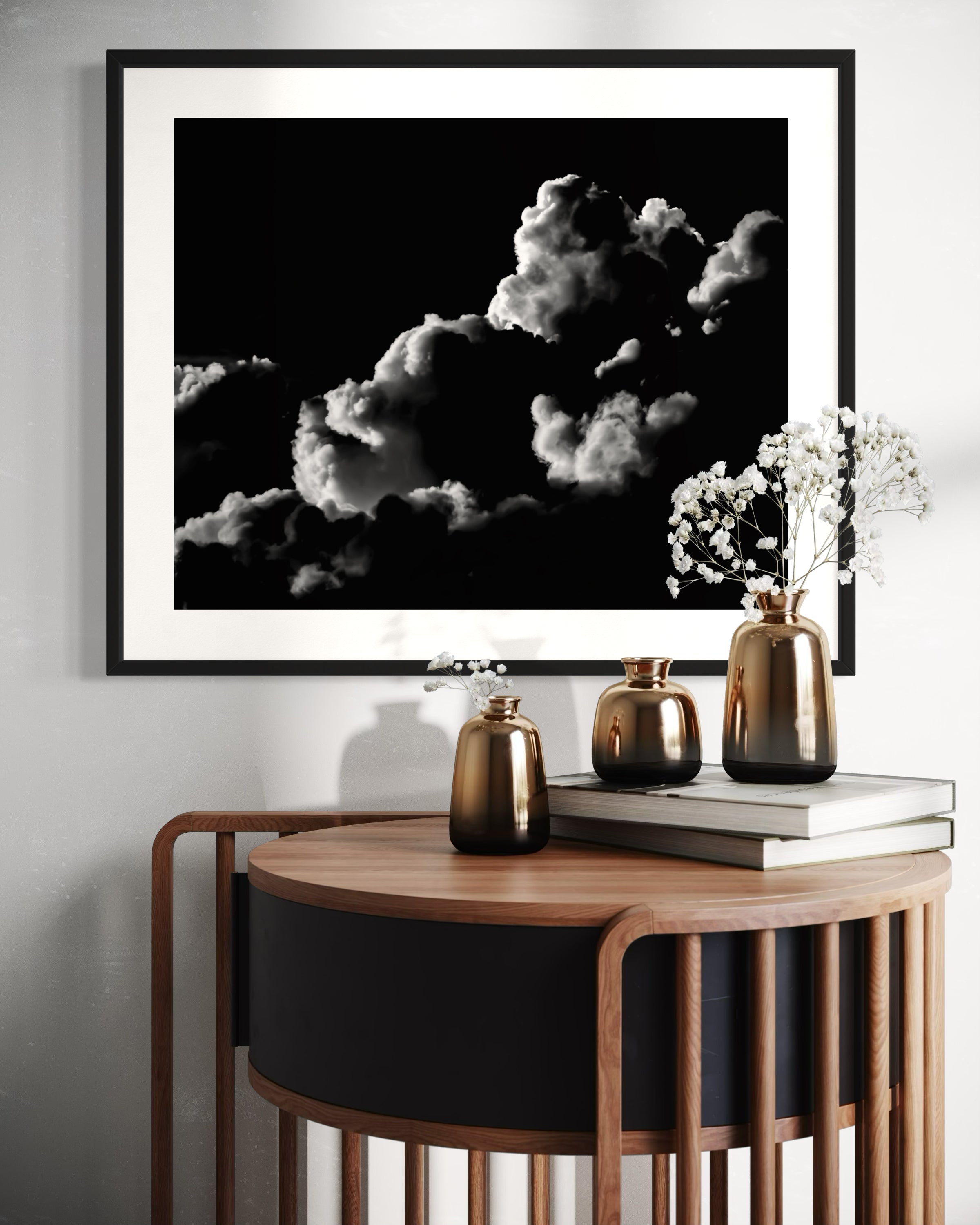 black and white photo of clouds, one looks like a dog's head in profile in black frame with white matte on white wall above small wooden table