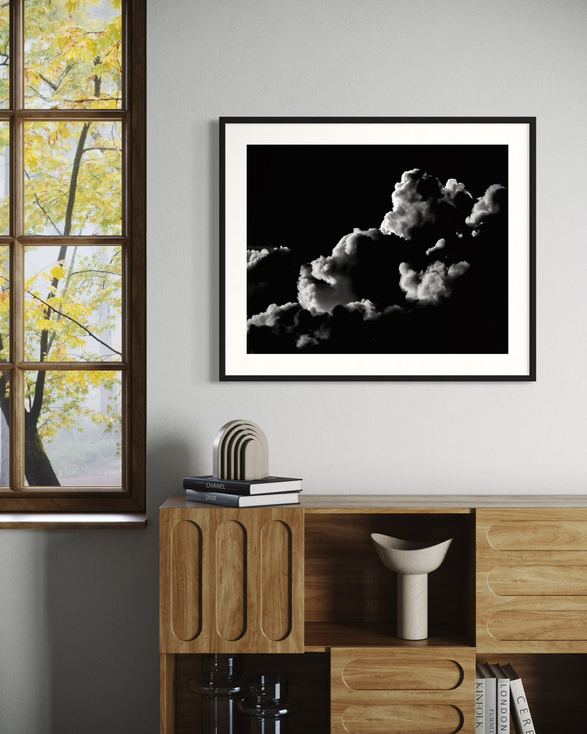 black and white photo of clouds, one looks like a dog's head in profile in black frame with white matte on off white wall in modern room