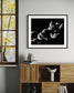 black and white photo of clouds, one looks like a dog's head in profile in black frame with white matte on off white wall in modern room