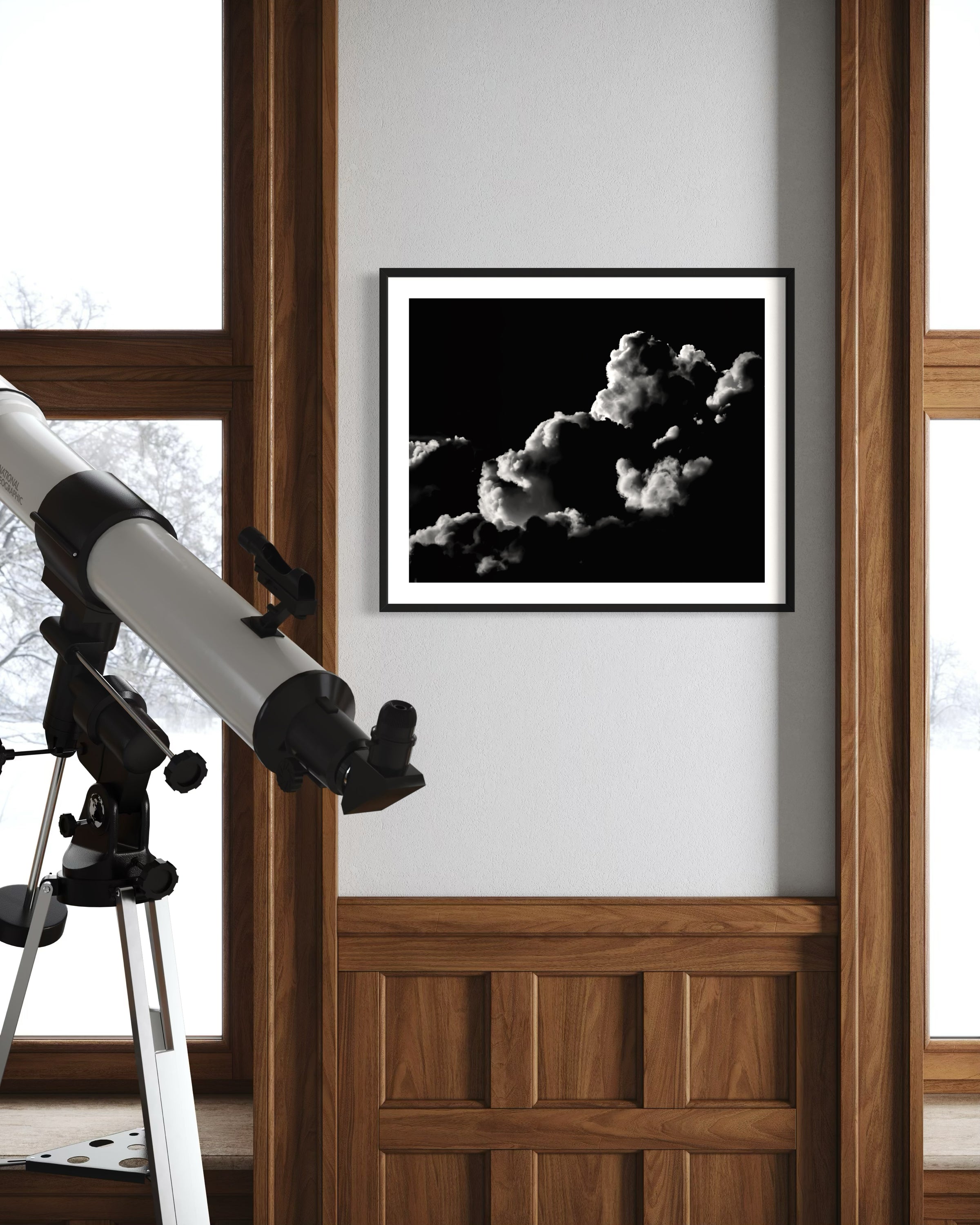 black and white photo of clouds, one looks like a dog's head in profile in black frame with white matte on off white wall in part of room with lots of wood trim and a telescope in the foreground 
