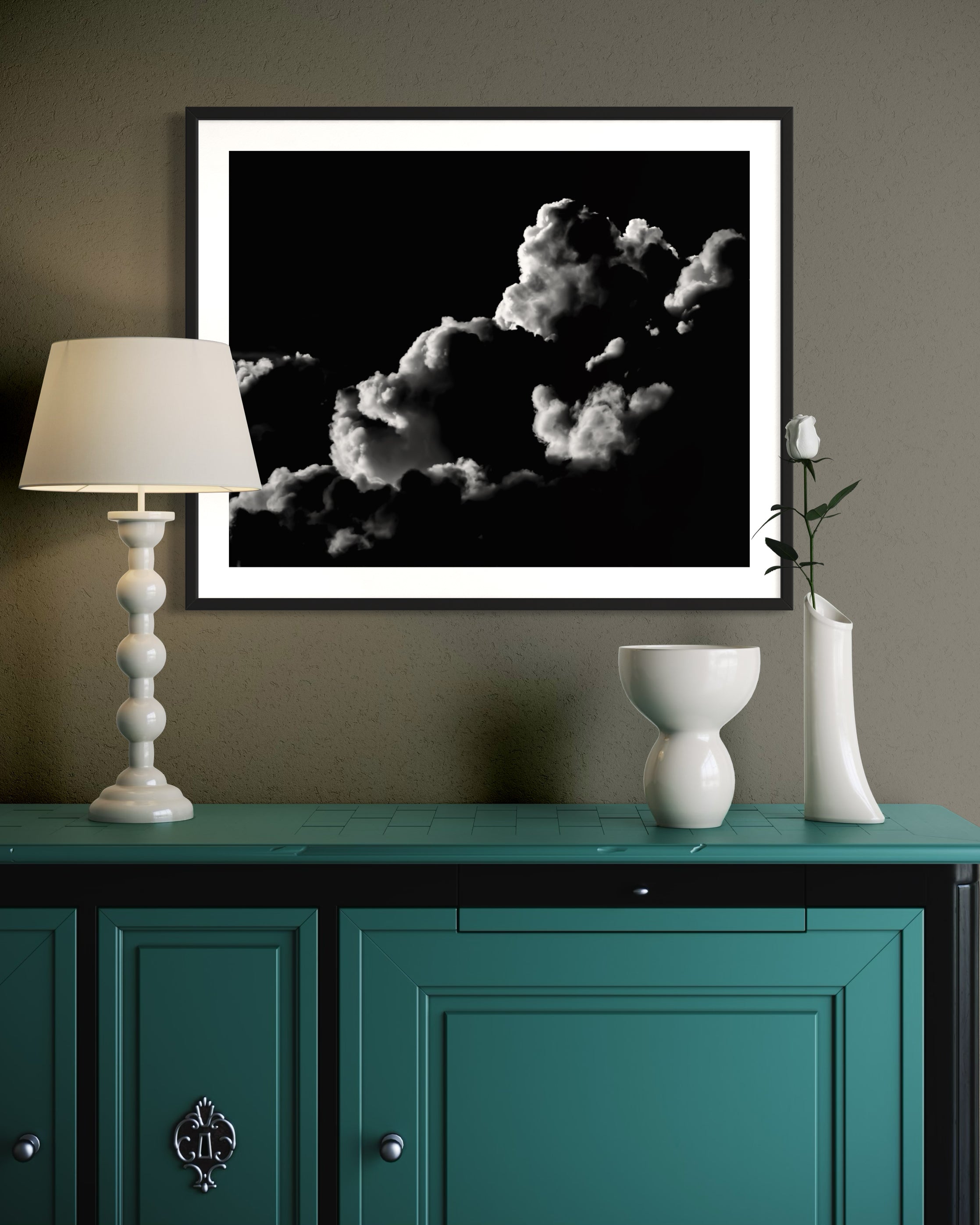 black and white photo of clouds, one looks like a dog's head in profile in black frame with white matte on warm gray wall above teal piece of furniture with lamp on top