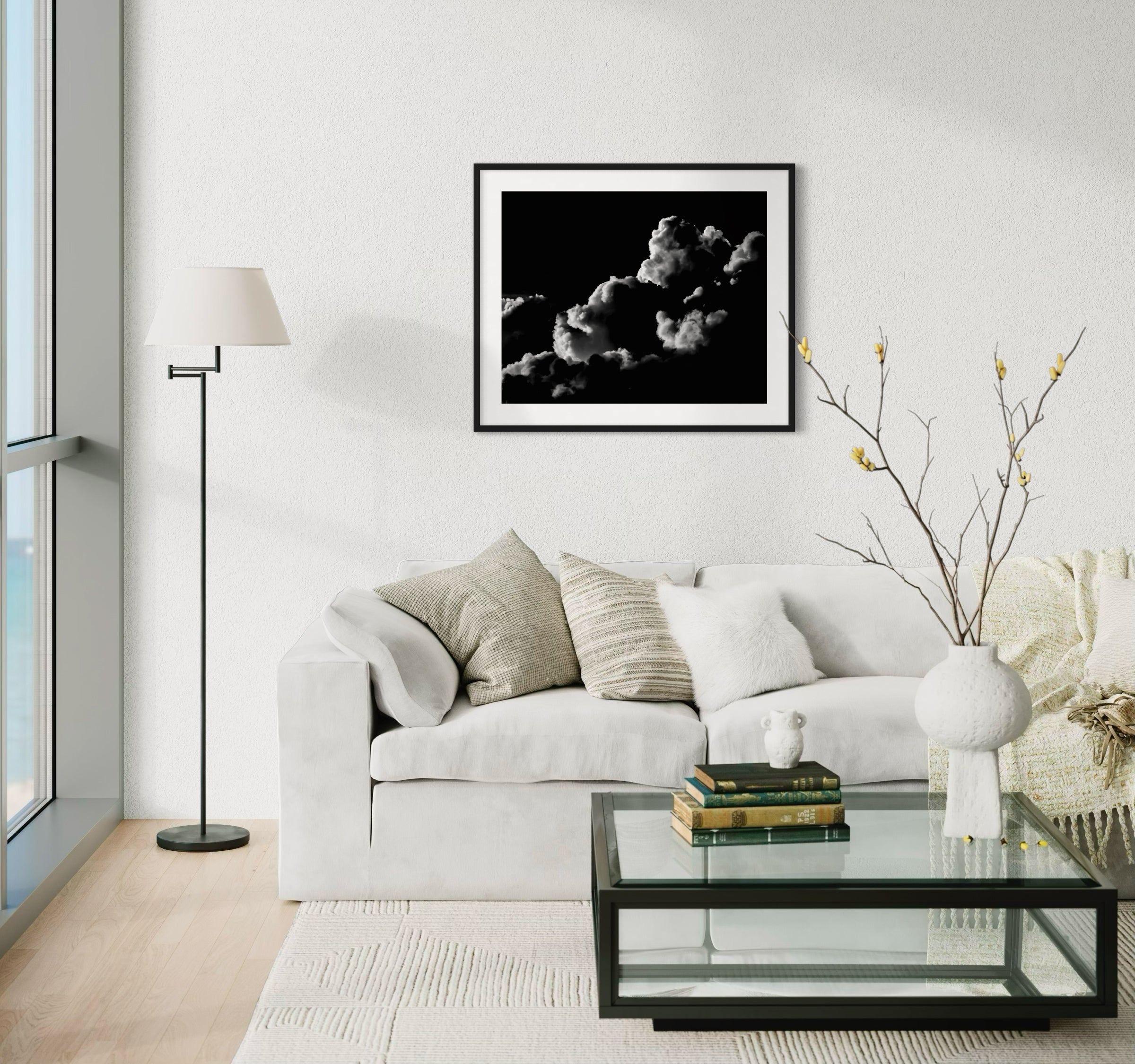 black and white photo of clouds, one looks like a dog's head in profile in black frame with white matte on off white wall in modern minimalist living room with white couch