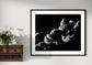 black and white photo of clouds, one looks like a dog's head in profile in black frame with white matte on off white wall with flowers on rustic shelf to the left