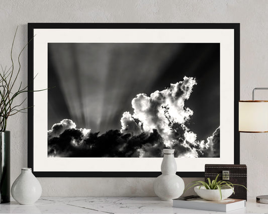 black and white photo of dramatic sky with some clouds and rays of light in black frame above white table