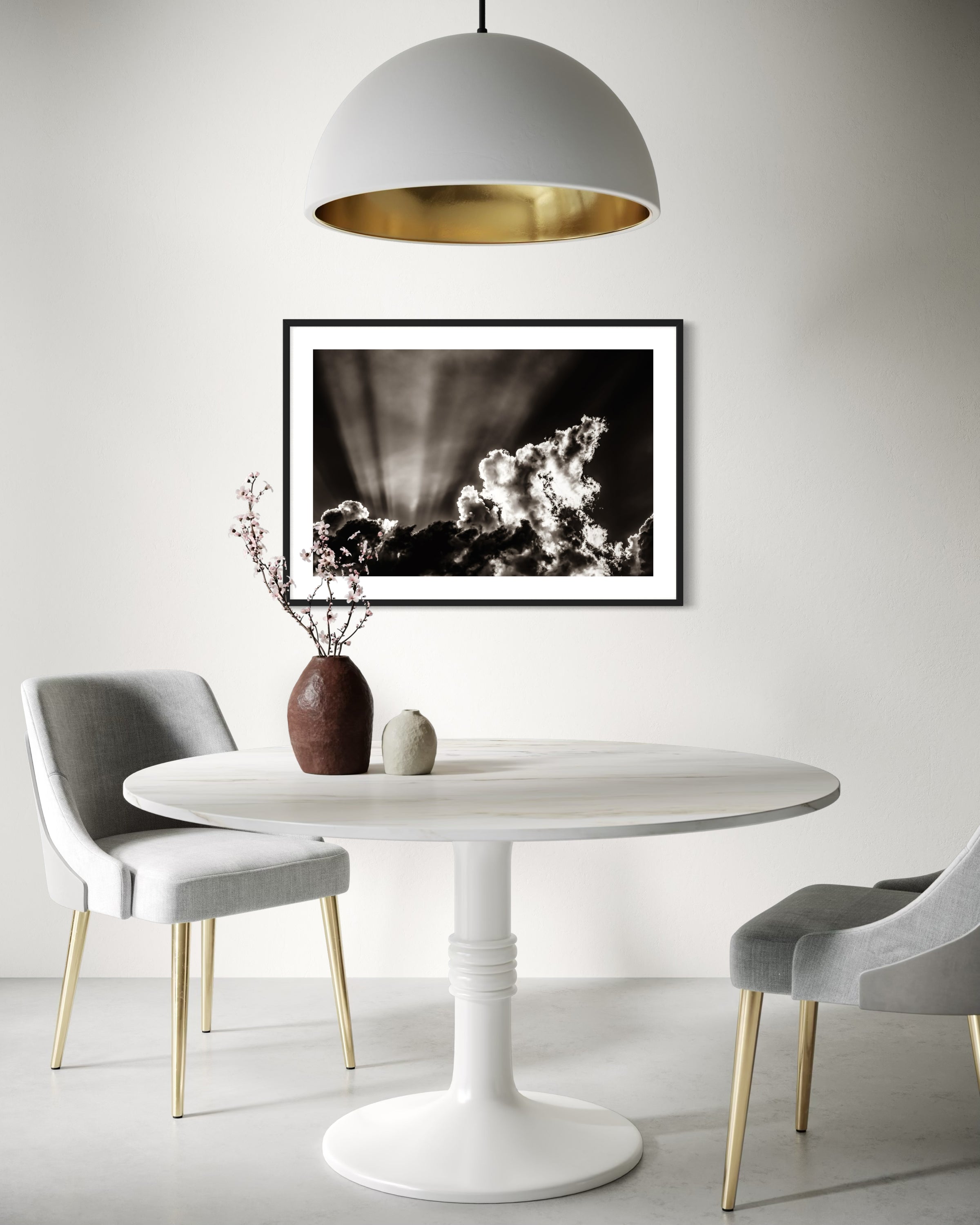 black and white photo of dramatic sky with some clouds and rays of light  in black frame with white matte on white wall in modern breakfast area with white and light gray tones 