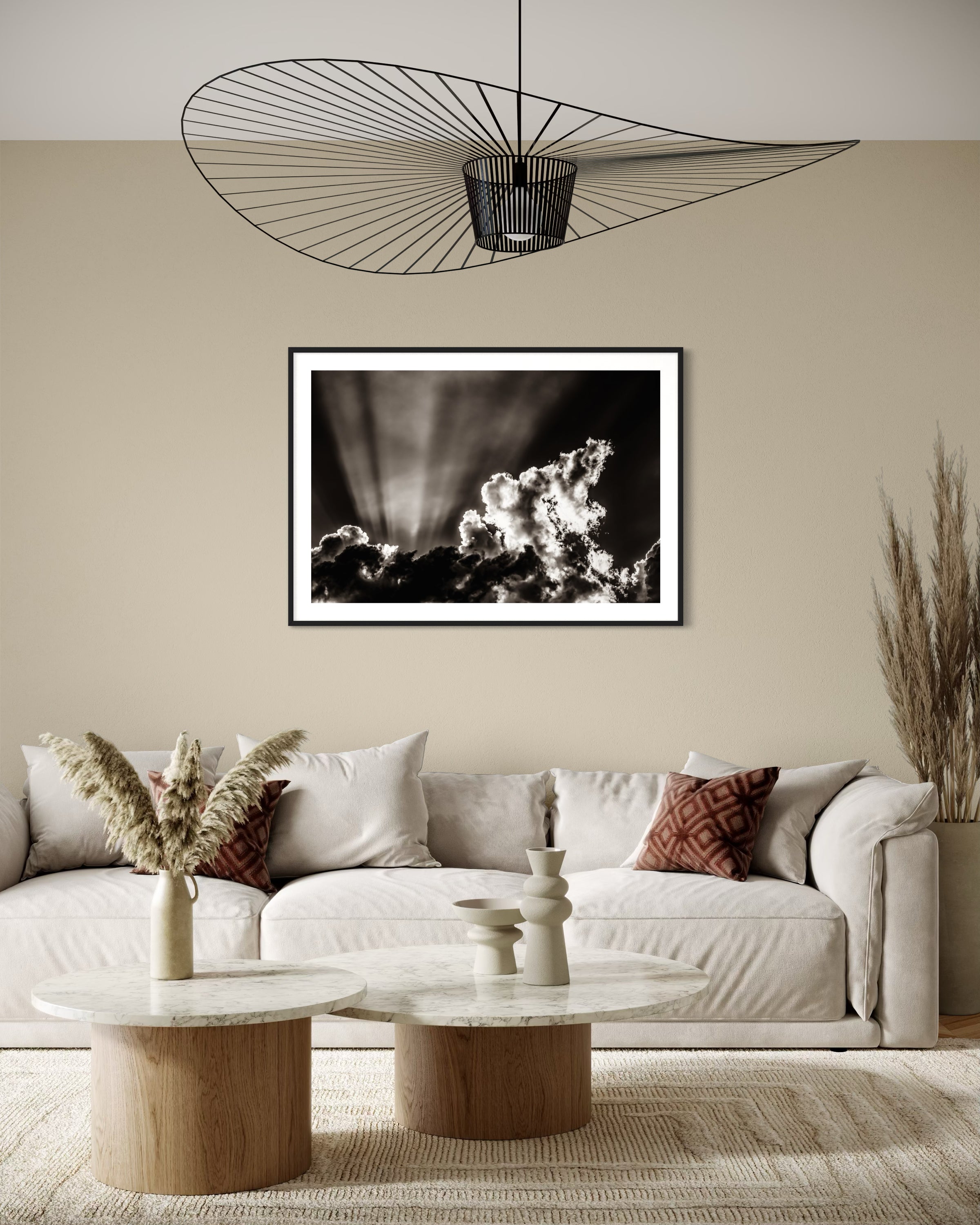 black and white photo of dramatic sky with some clouds and rays of light  in black frame with white matte on tan wall in earth toned living room with off white couch