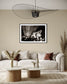 black and white photo of dramatic sky with some clouds and rays of light  in black frame with white matte on tan wall in earth toned living room with off white couch