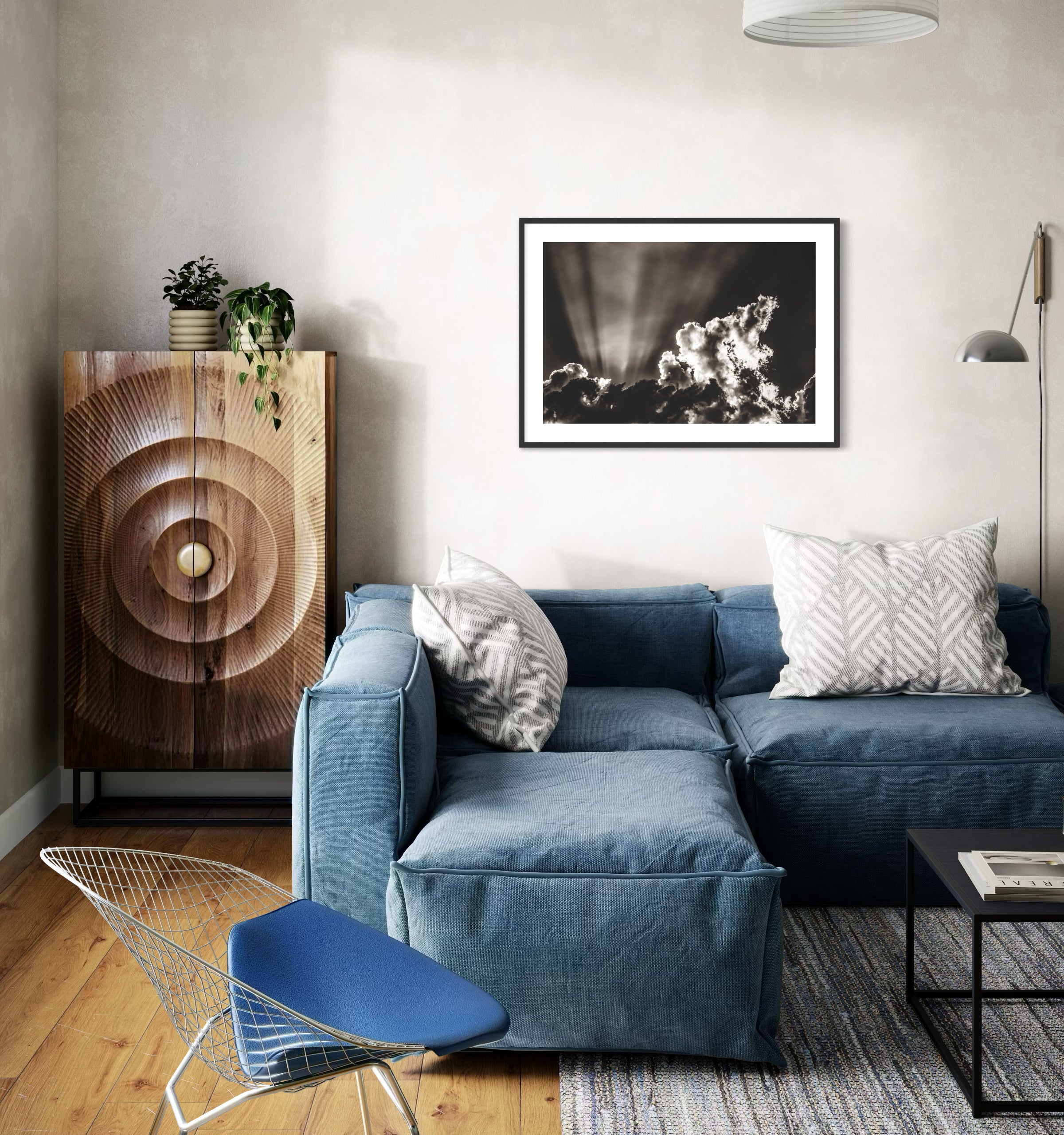 black and white photo of dramatic sky with some clouds and rays of light  in black frame with white matte on white wall in eclectic relaxed living room with denim couch and hardwood floors