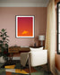warm tone photo of single cloud in black frame with white matte on light pale pink wall above wooden desk in home office with colorful rug and one tall green plant