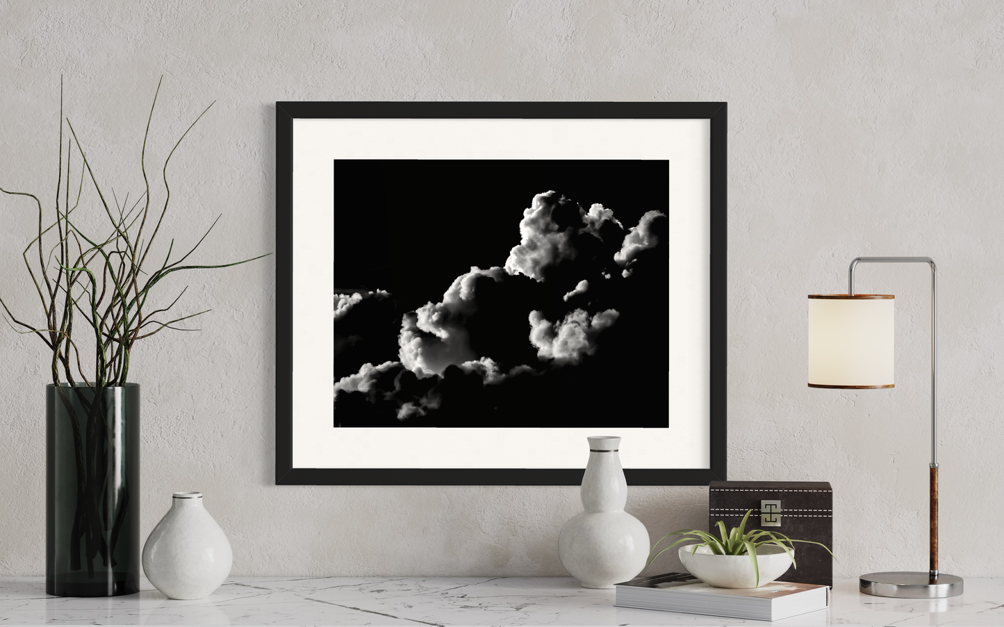 black and white photo of clouds, one looks like a dog's head in profile in black frame on white wall above modern table