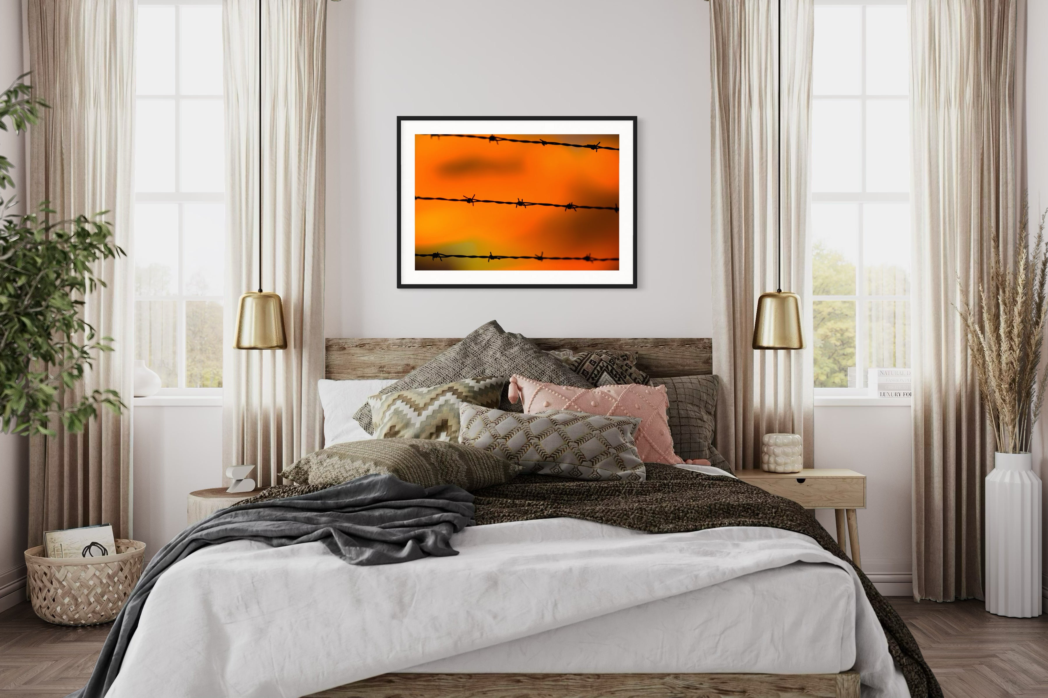 Close up of barbed wire fence with sunset in the background, in black frame with white matte on tan wall above bed in rustic bedroom with hardwood floors