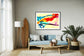 swirls of blue, yellow, orange, teal, purple and red on light yellow background in black frame with off white matte on light gray wall in modern home living room