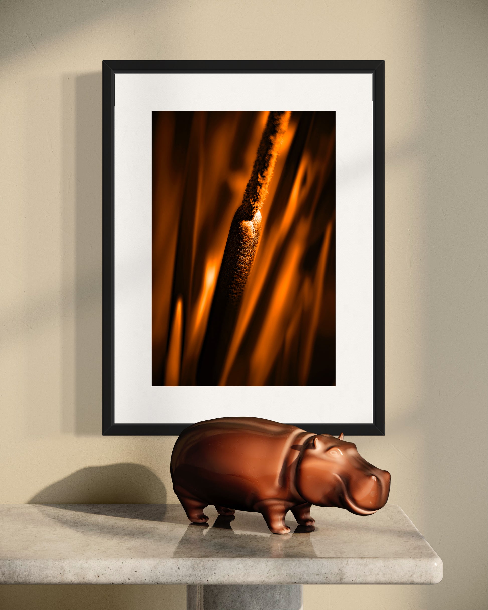 reeds in gold tone with selective focus photo in black frame on tan wall with hippo ceramic on concrete table