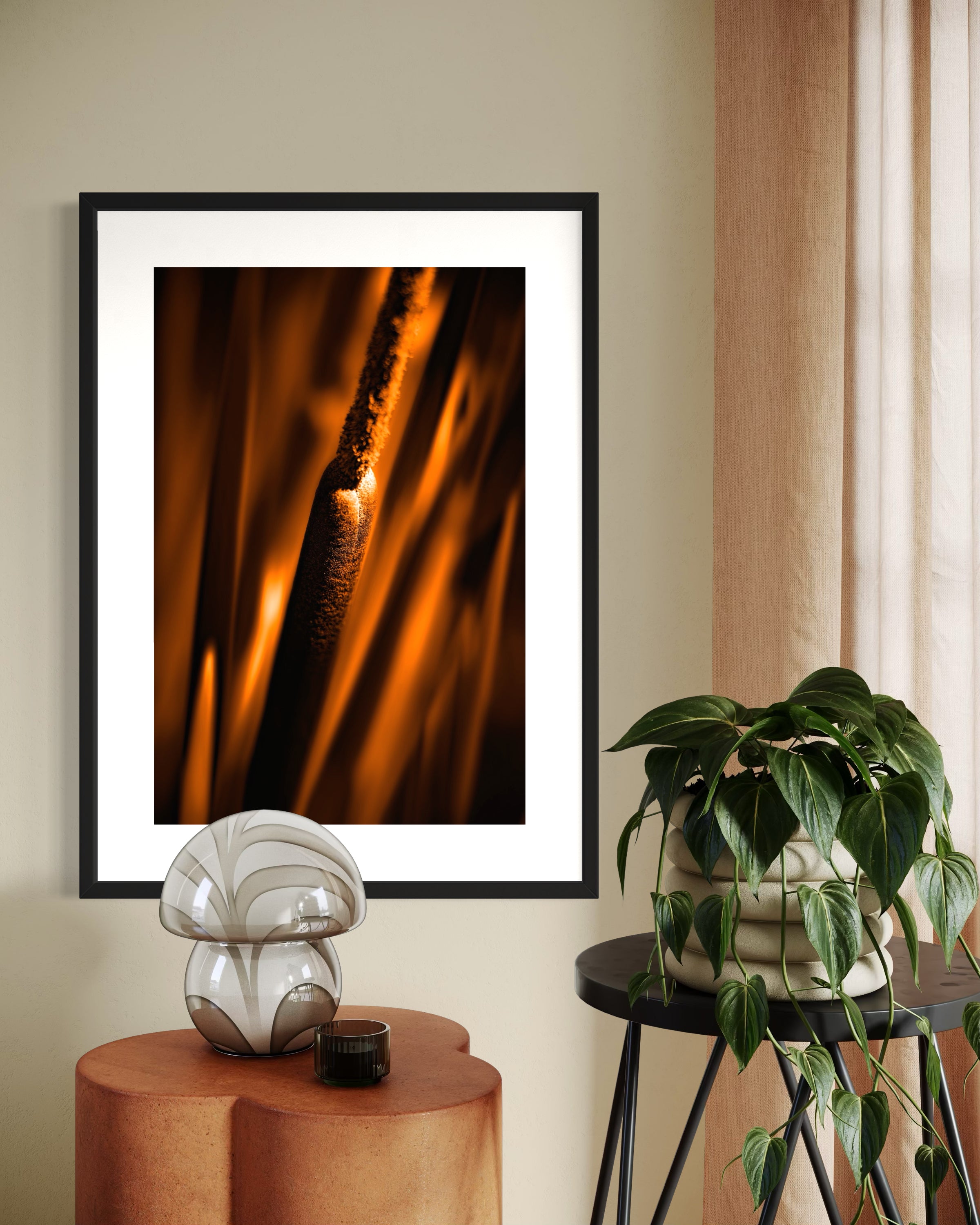 reeds in gold tone with selective focus photo in black frame with white matte on tan wall above small dark wooden table and green plant