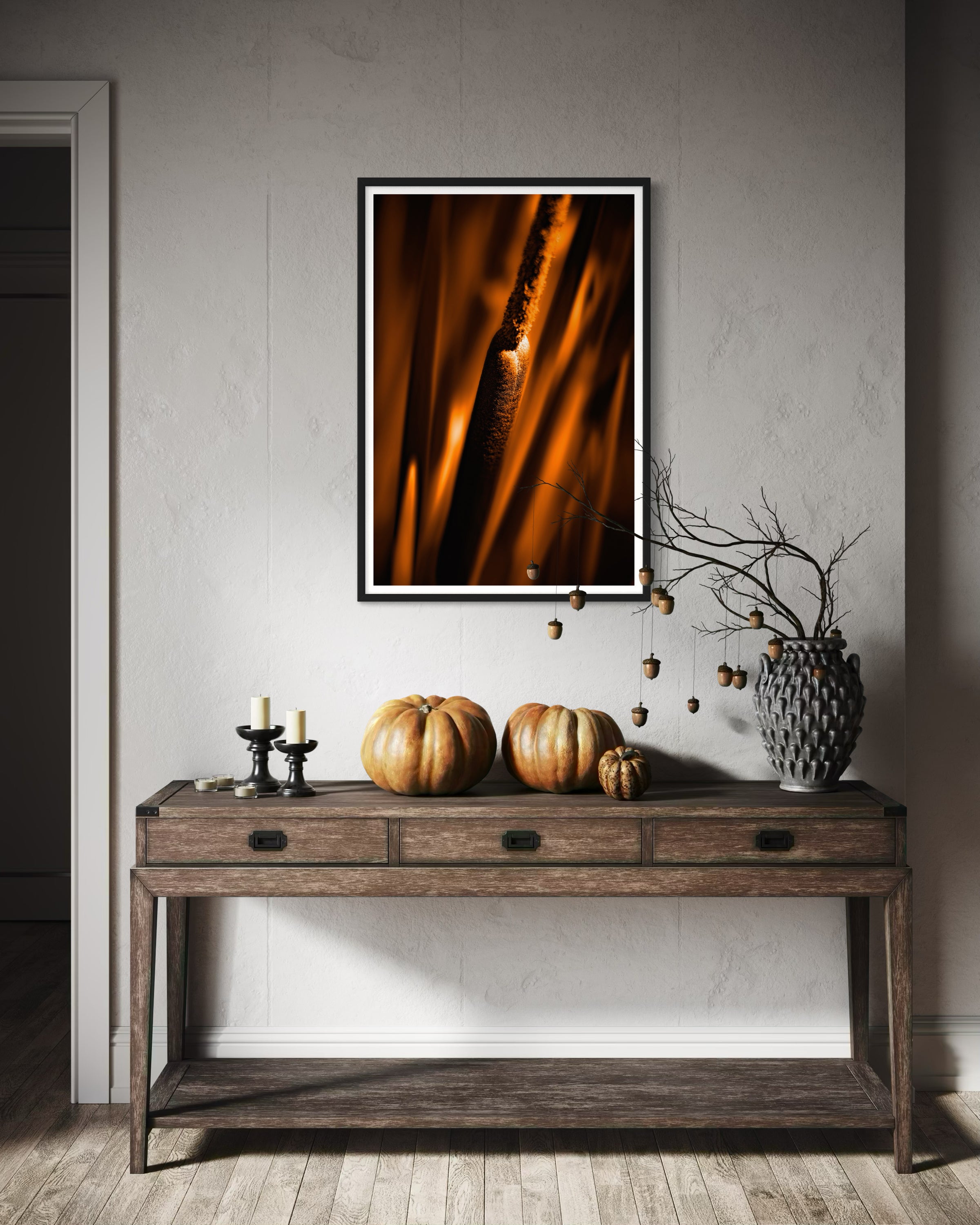 reeds in gold tone with selective focus photo in black frame with white matte on tan wall above rustic dark wooden table with drawers