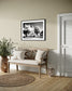a black and white photo of a building with trees in front in black frame with white matte on tan wall in country style sitting area with hardwood floors