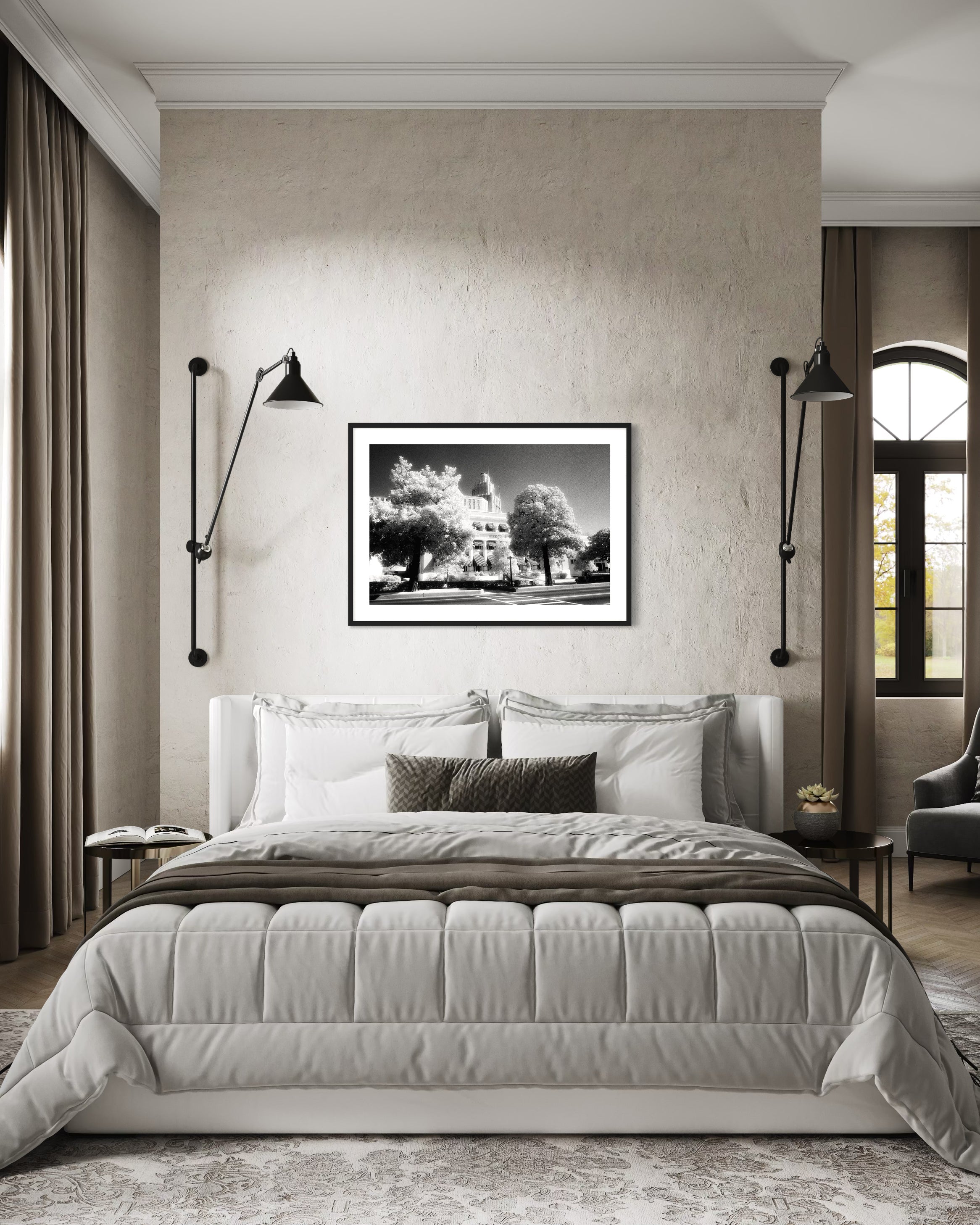 a black and white photo of a building with trees in front in black frame with white matte on light tan wall above bed in rustic earth toned bedroom
