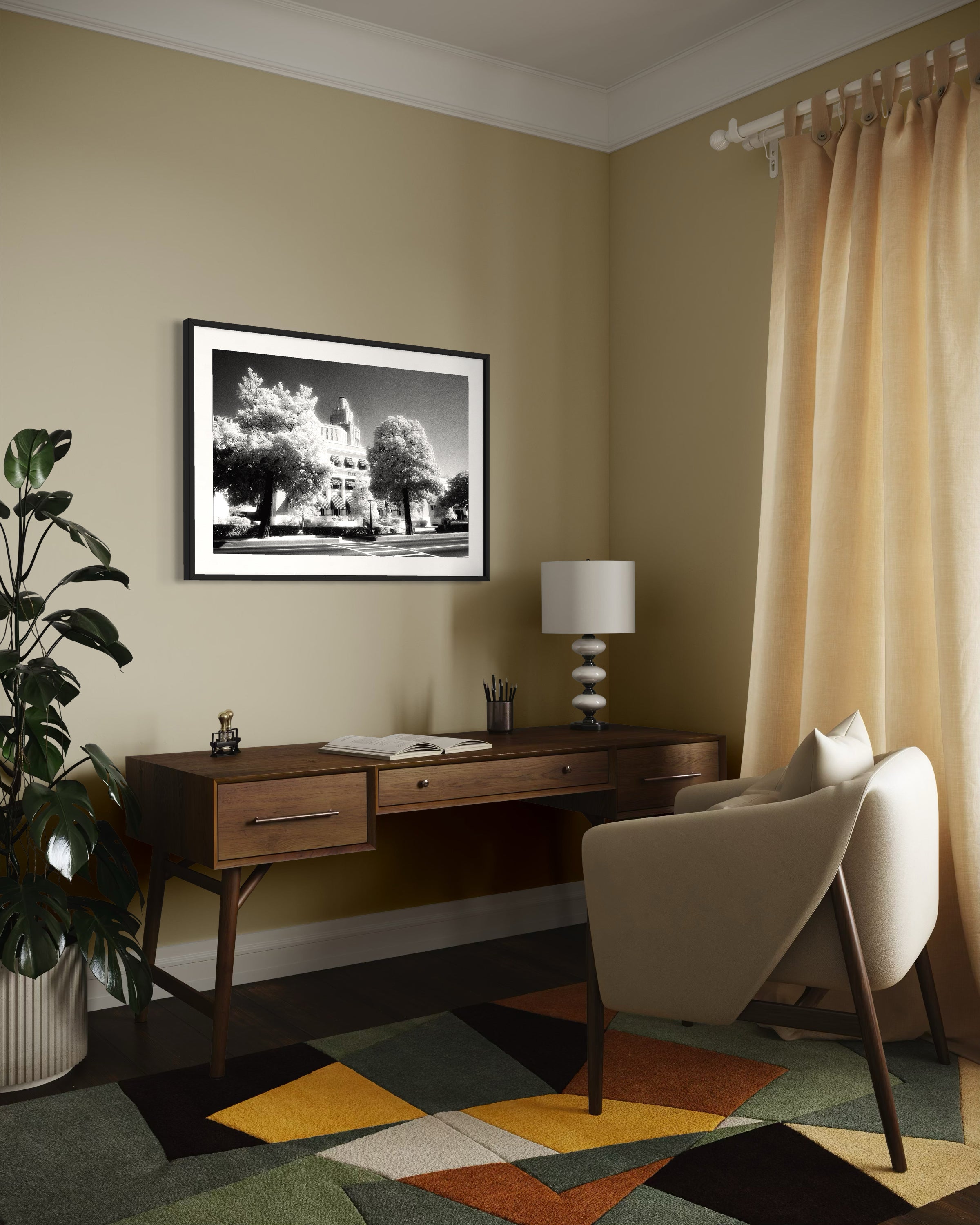 a black and white photo of a building with trees in front in black frame with white matte on tan wall in modern home office with wooden desk, white chair and colorful rung