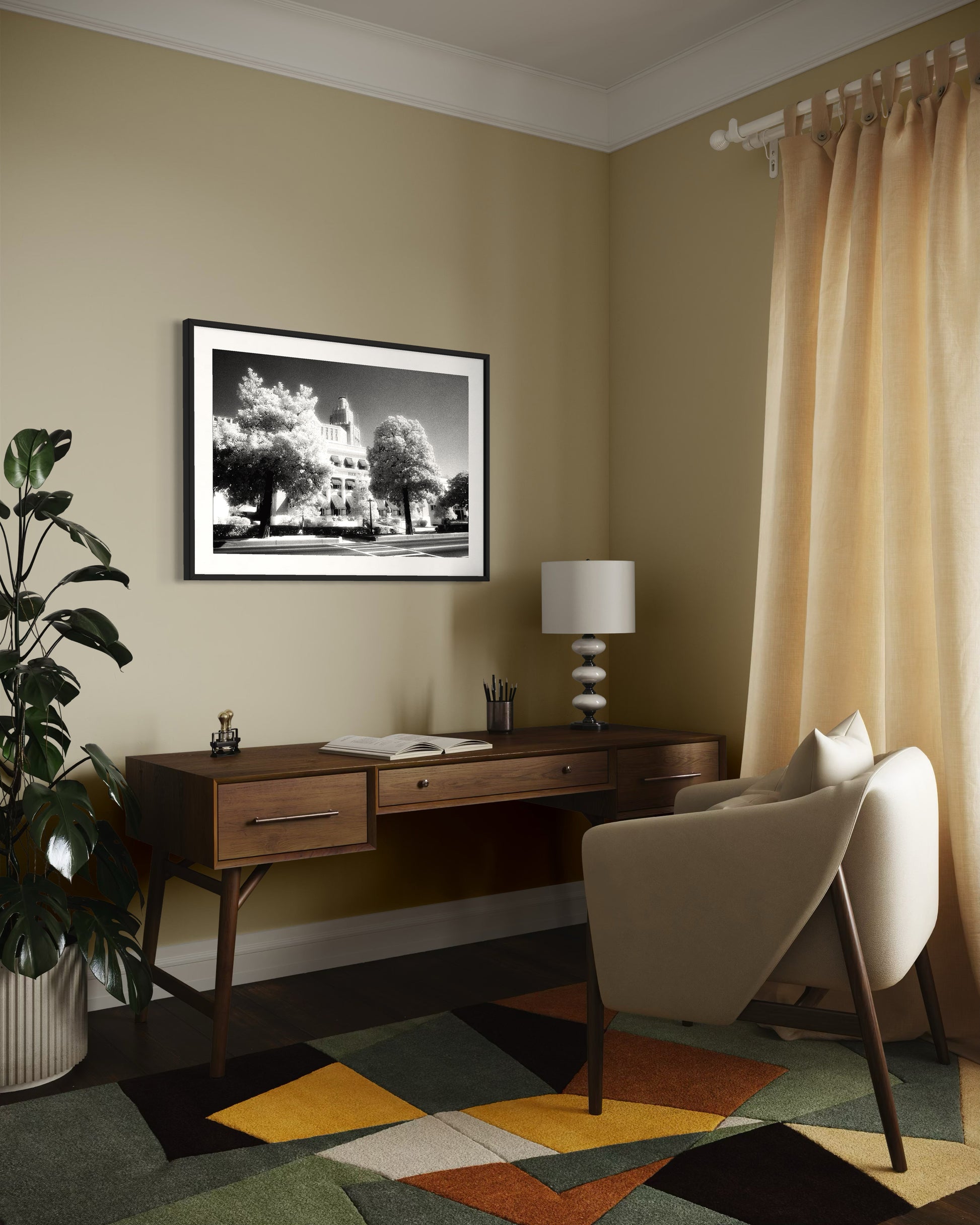 a black and white photo of a building with trees in front in black frame with white matte on tan wall in modern home office with wooden desk, white chair and colorful rung