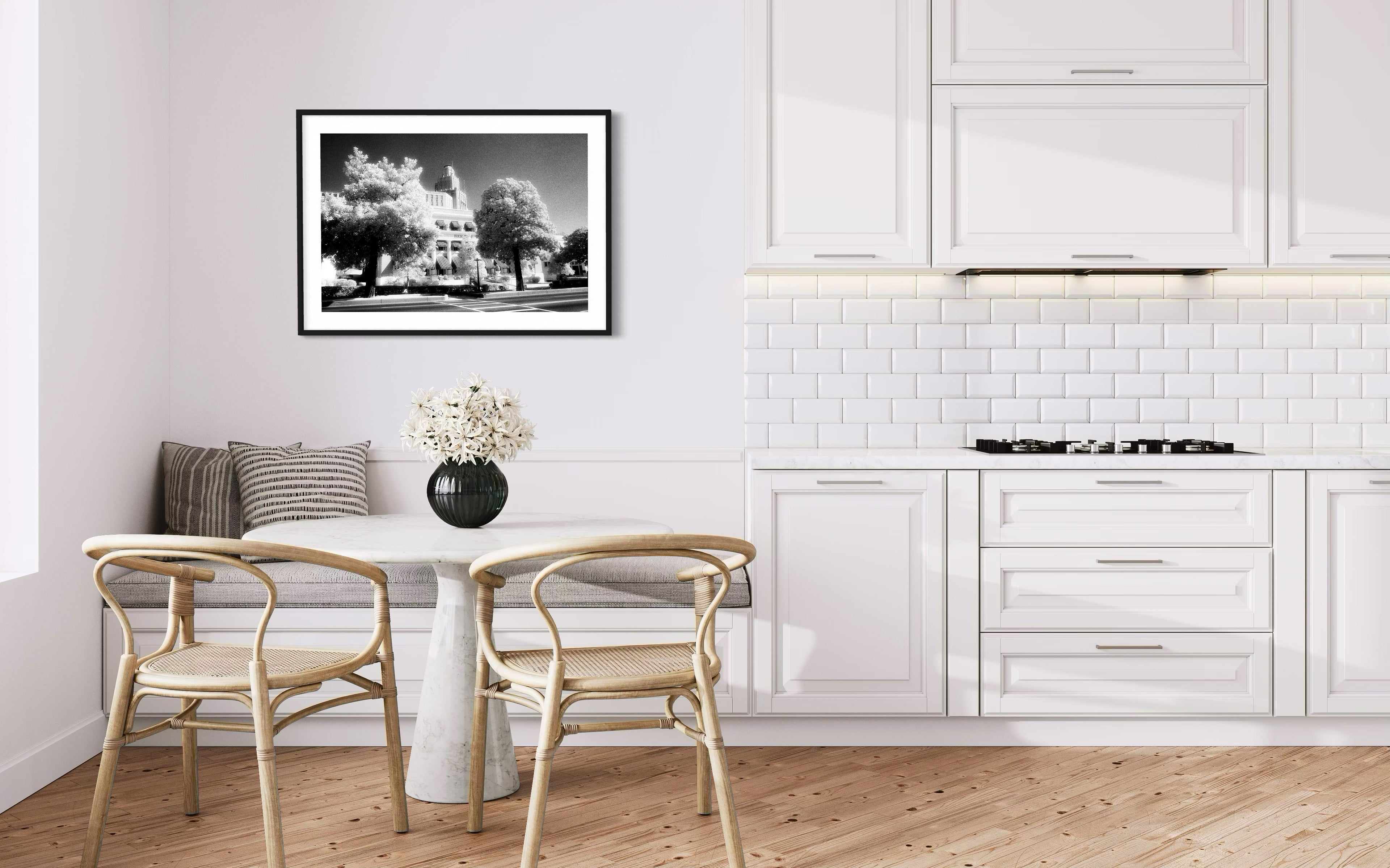 Modern kitchen with white cabinetry, wooden floor, and a framed black and white photo on the wall.