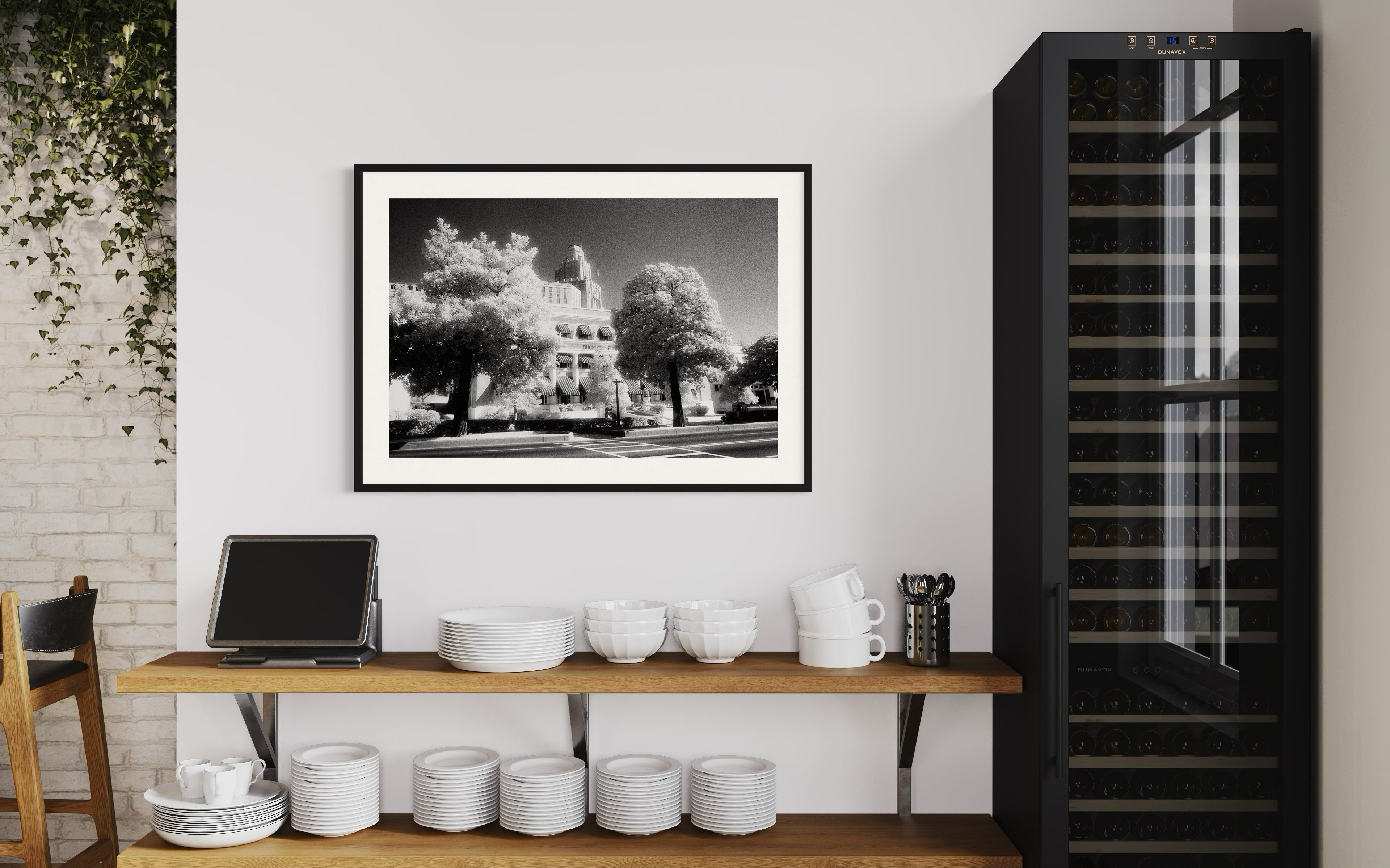 Modern kitchen interior with a framed black and white photo, shelves with kitchenware, and a wine cooler.