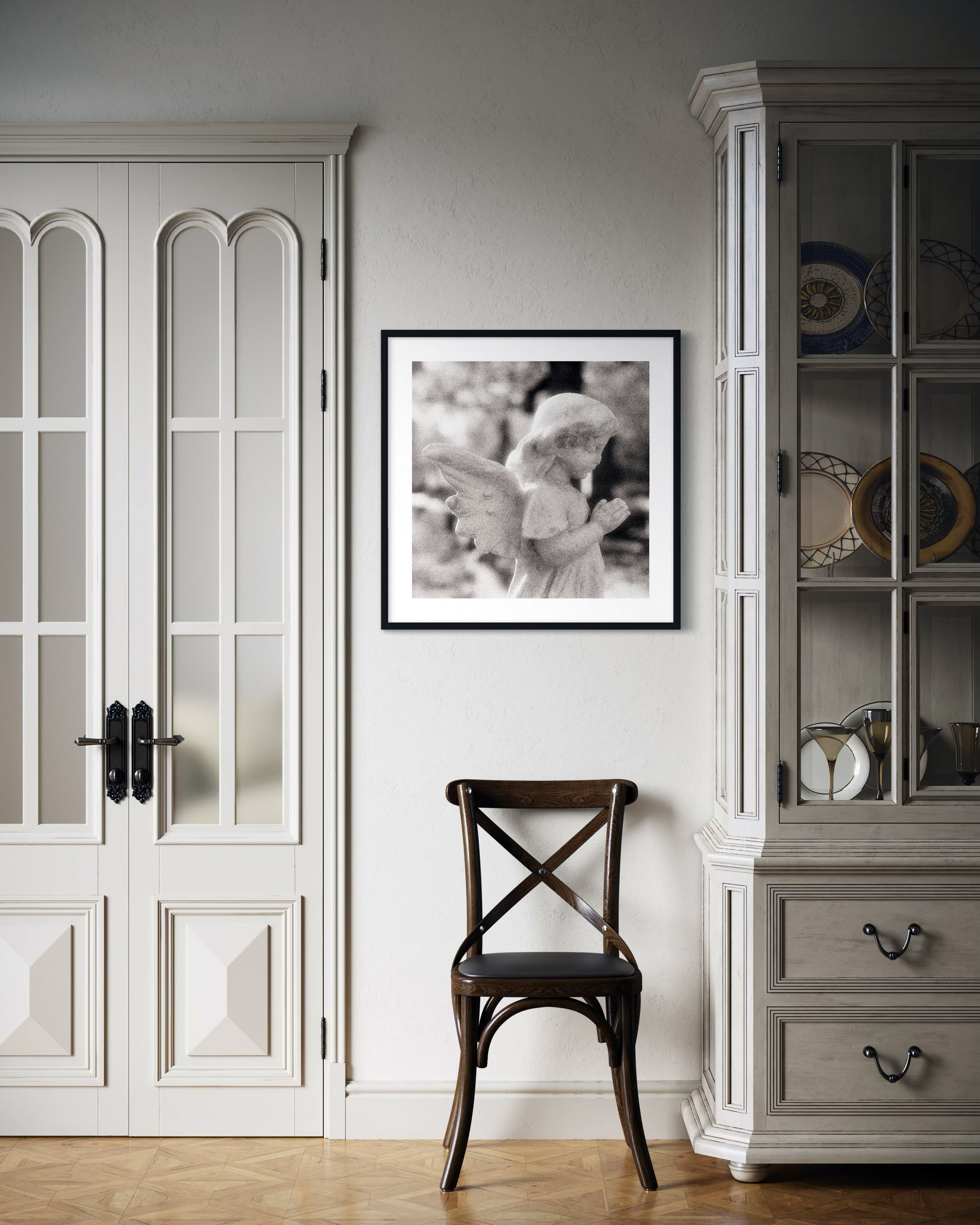 cherub statue with hands in praying position in sepia tone in black frame with white matte on light gray wall in classic style home with tan tones and hardwood floors