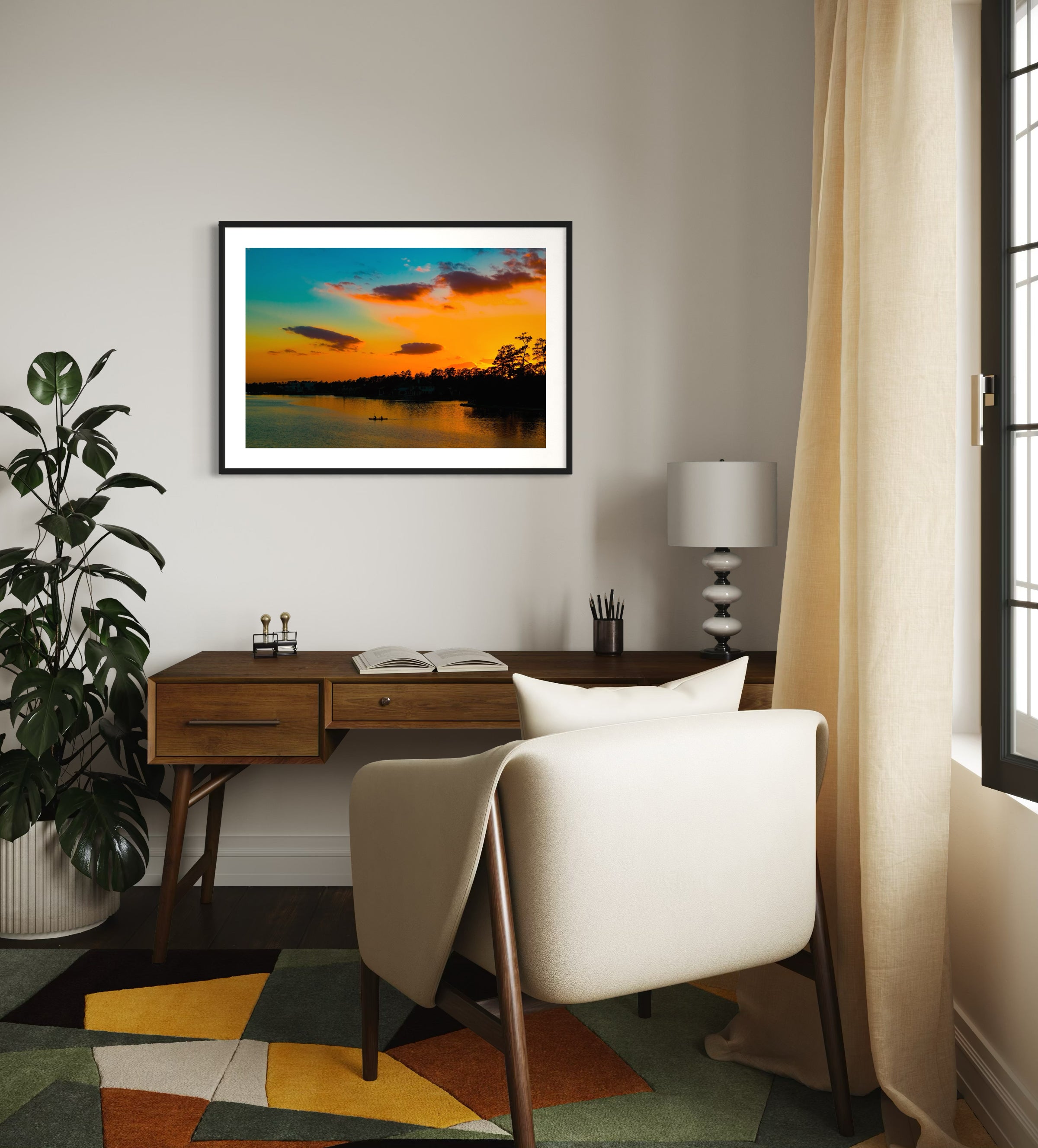 wide angle photo of kayak on lake at sunset in black frame with white matte above wooden desk with white chair in home office