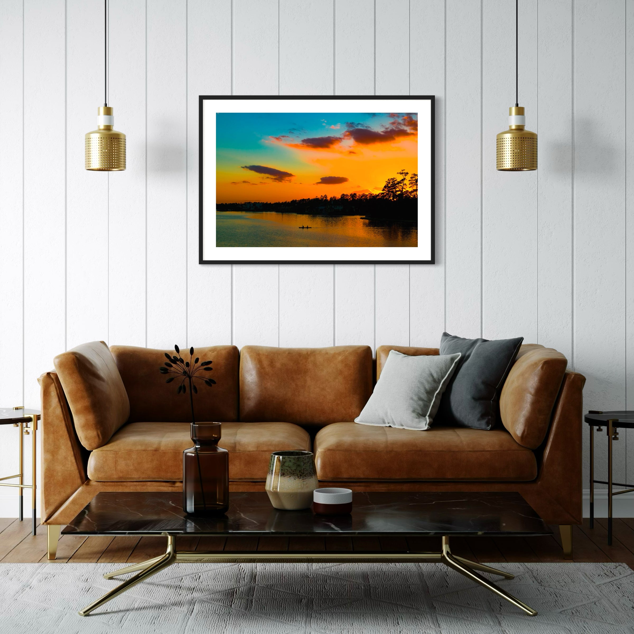 wide angle photo of kayak on lake at sunset in black frame with white matte on off white wall in eclectic living room with brown leather couch and wood floors