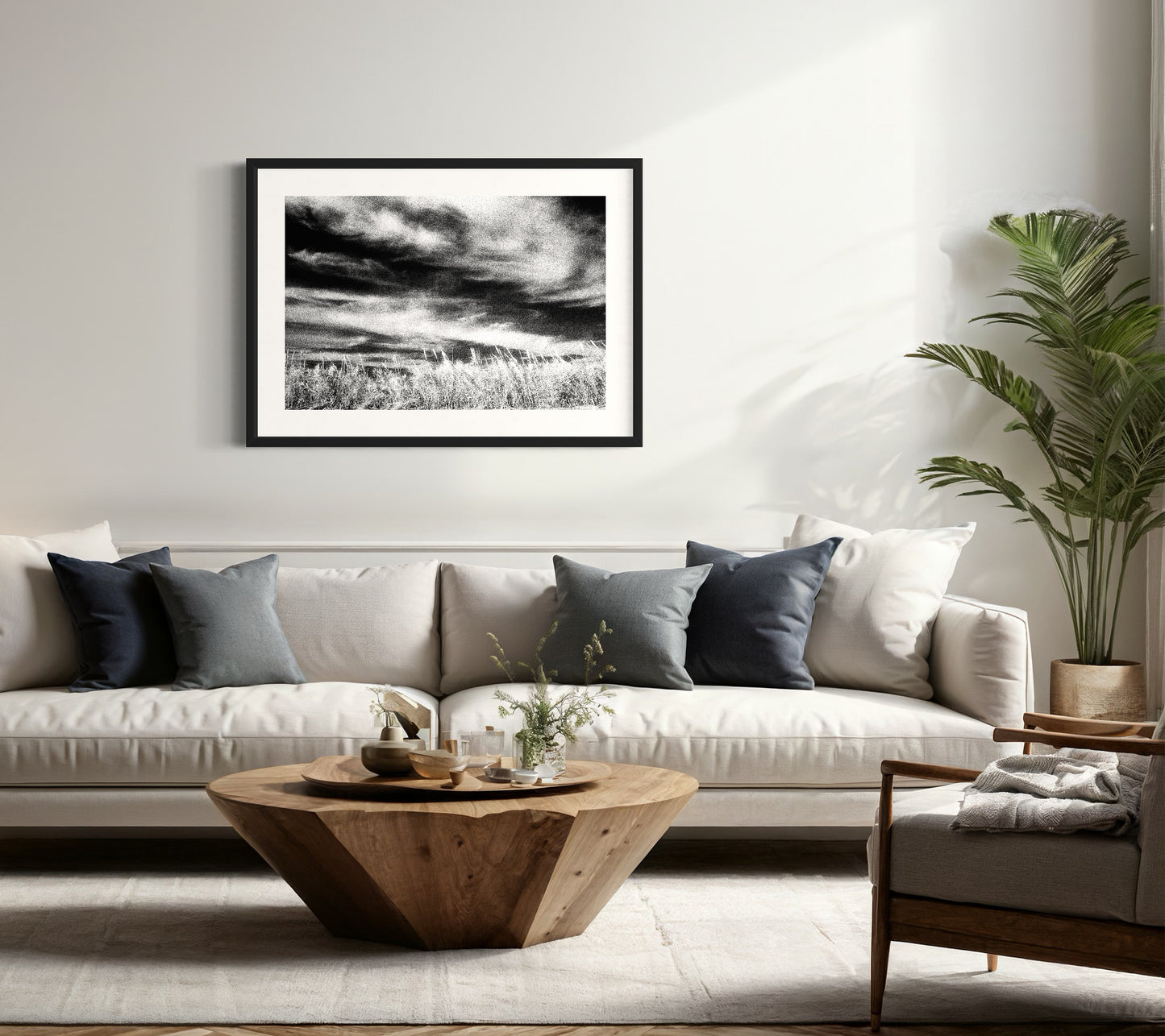 black and white photo of long clouds and plants with stalks in the foreground in black frame with white matte above sofa in relaxed, nature toned living room