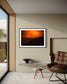photo of orange haze in sky over shallow mountains in black frame with white matte on tan wall in sitting room in modern house