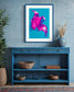 bright pop art photo of pink lily on blue background in blue frame above small blue table in rustic room with blue walls