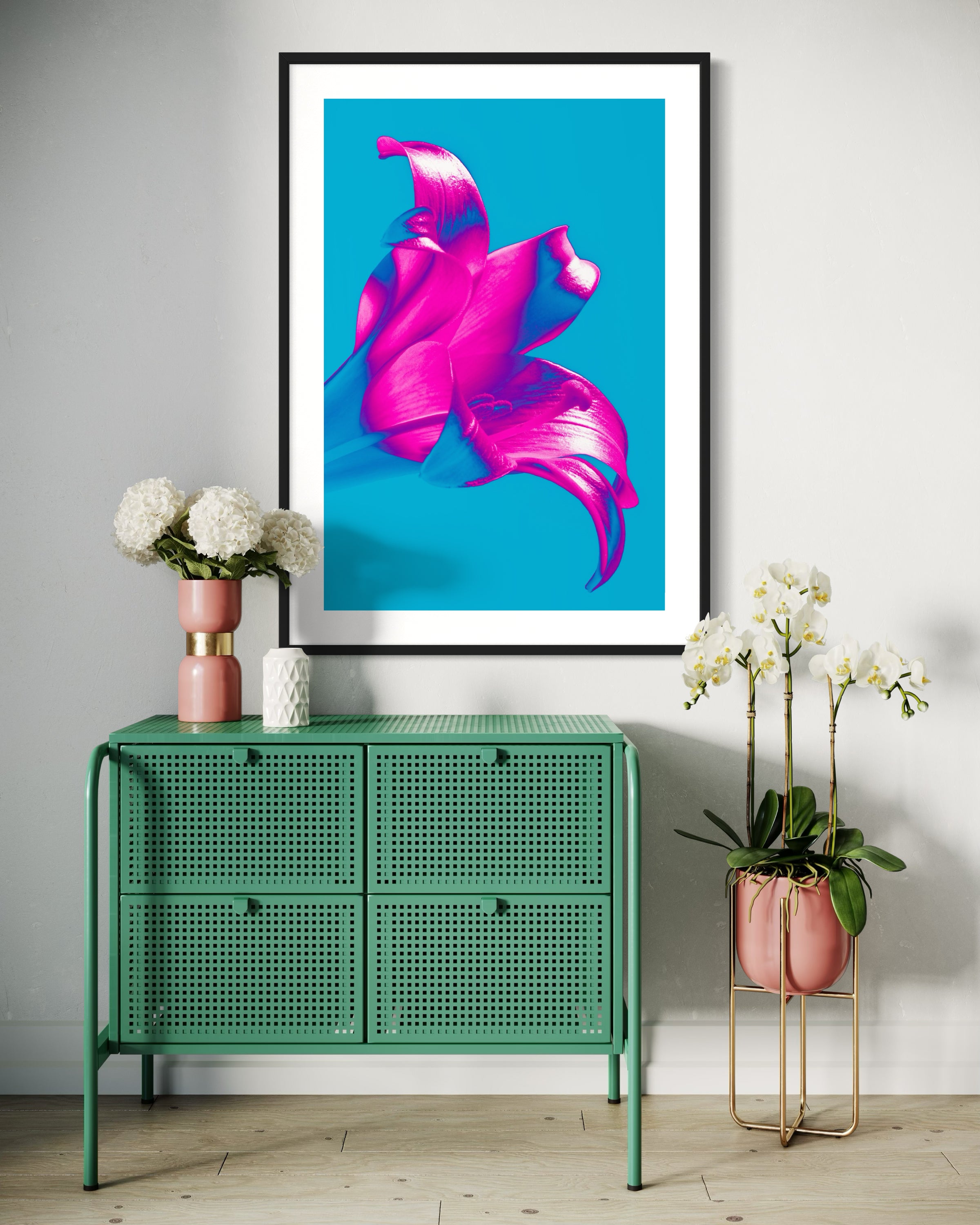bright pop art photo of pink lily on blue background in black frame with white matte on light gray wall above small green metal table with flowers on top and on the side