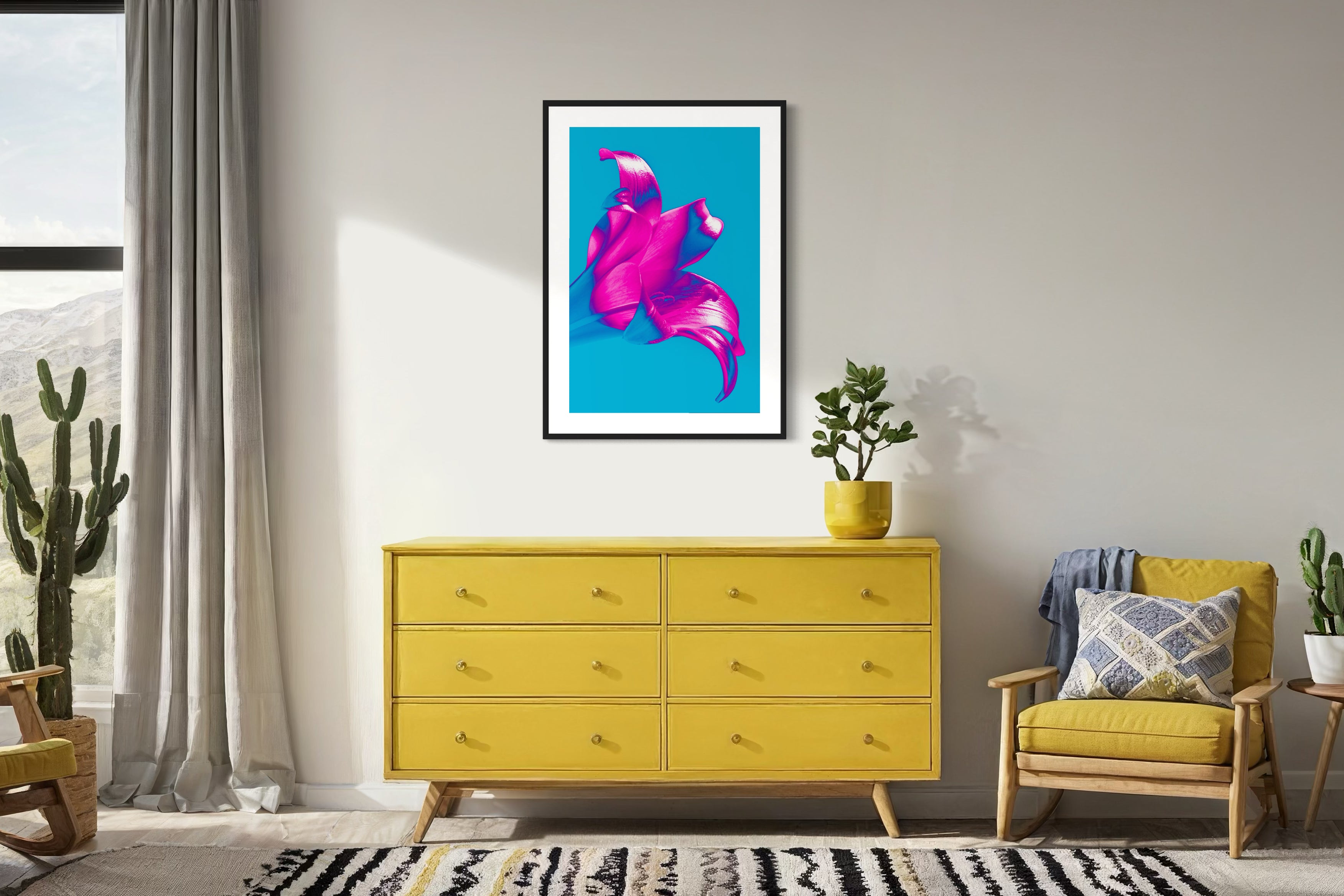 bright pop art photo of pink lily on blue background in black frame with white matte on light tan wall yellow chest of drawers with yellow chair on the side