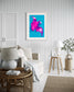 bright pop art photo of pink lily on blue background in gray frame with light gray matte in coastal style sitting room with white and tones