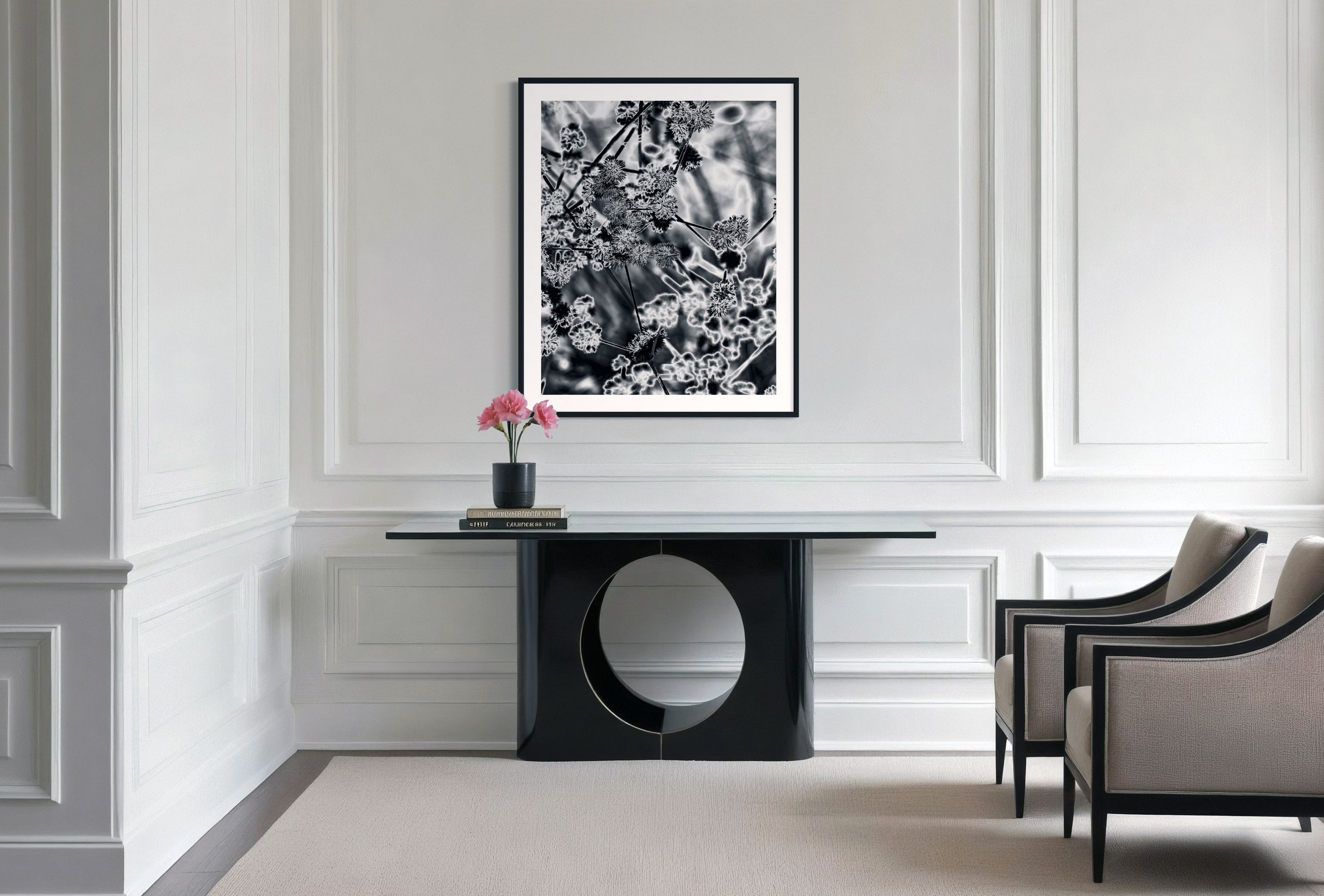 black and white close up of plant with solarized effect in black frame with white matte above small wide modern black table in minimalist sitting area