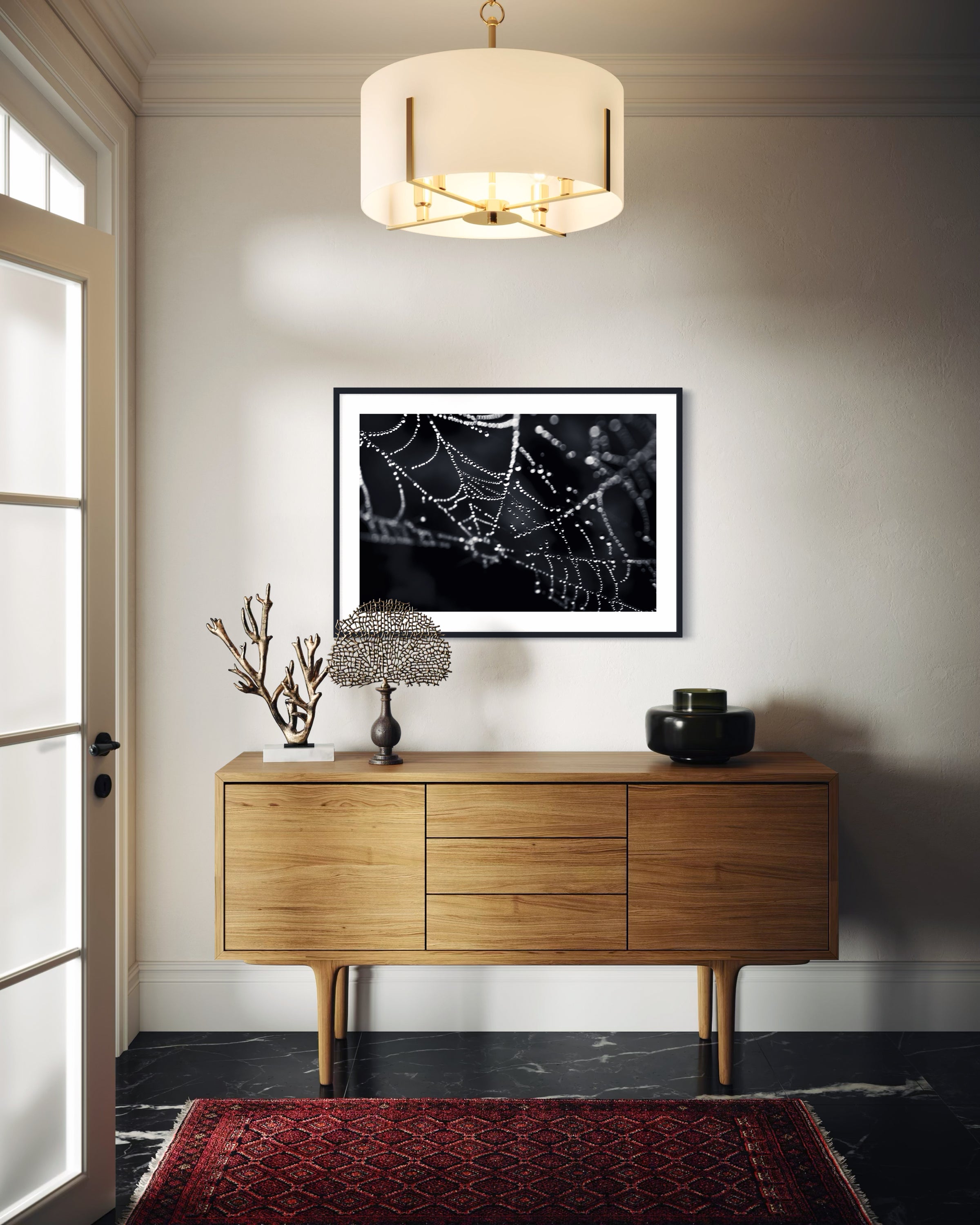 close up photo of rain drops on spider web in black and white in black frame with white matte on white wall above modern wooden piece of furniture