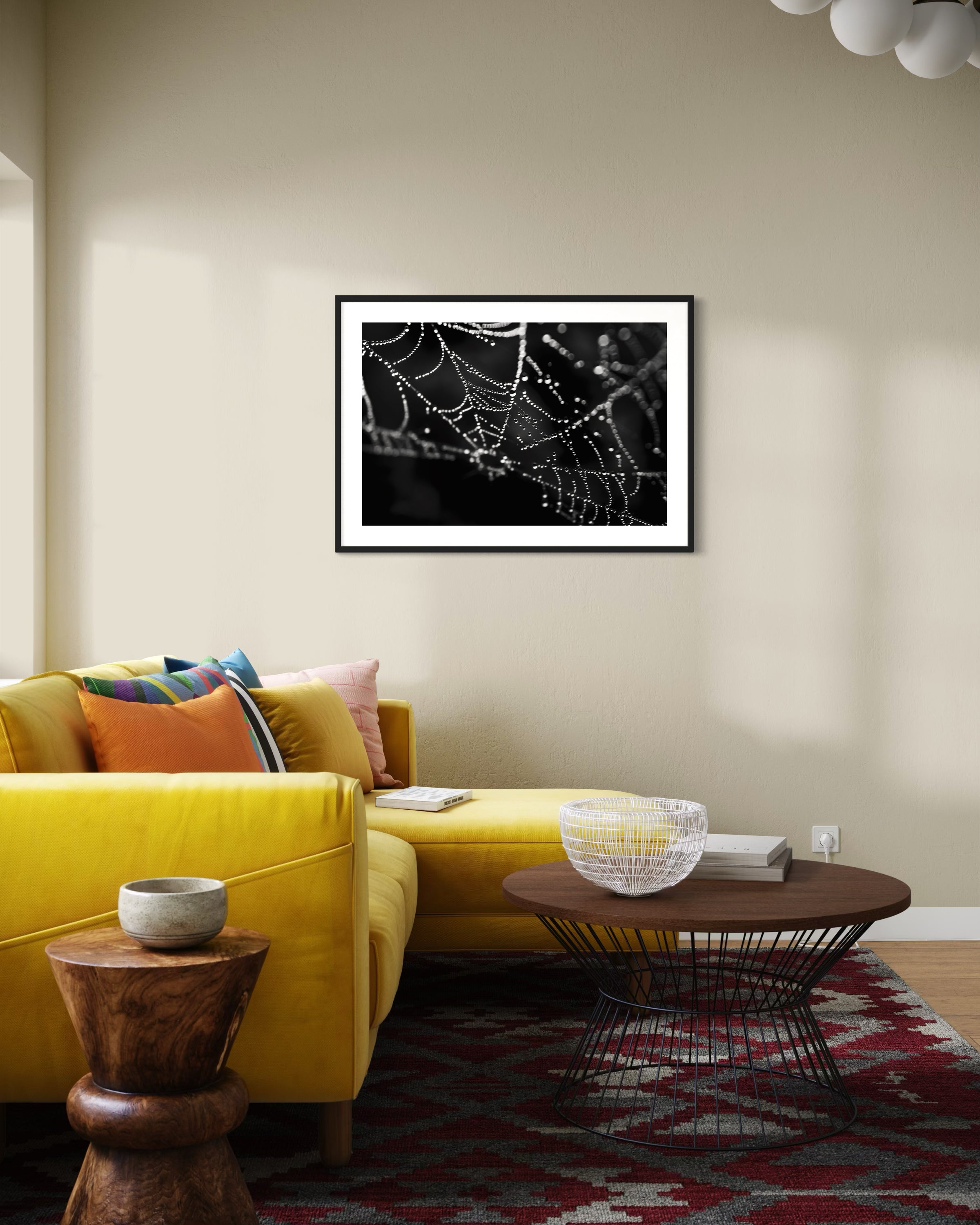 close up photo of rain drops on spider web in black and white in black frame with white matte on light tan wall in modern living room with bright yellow couch