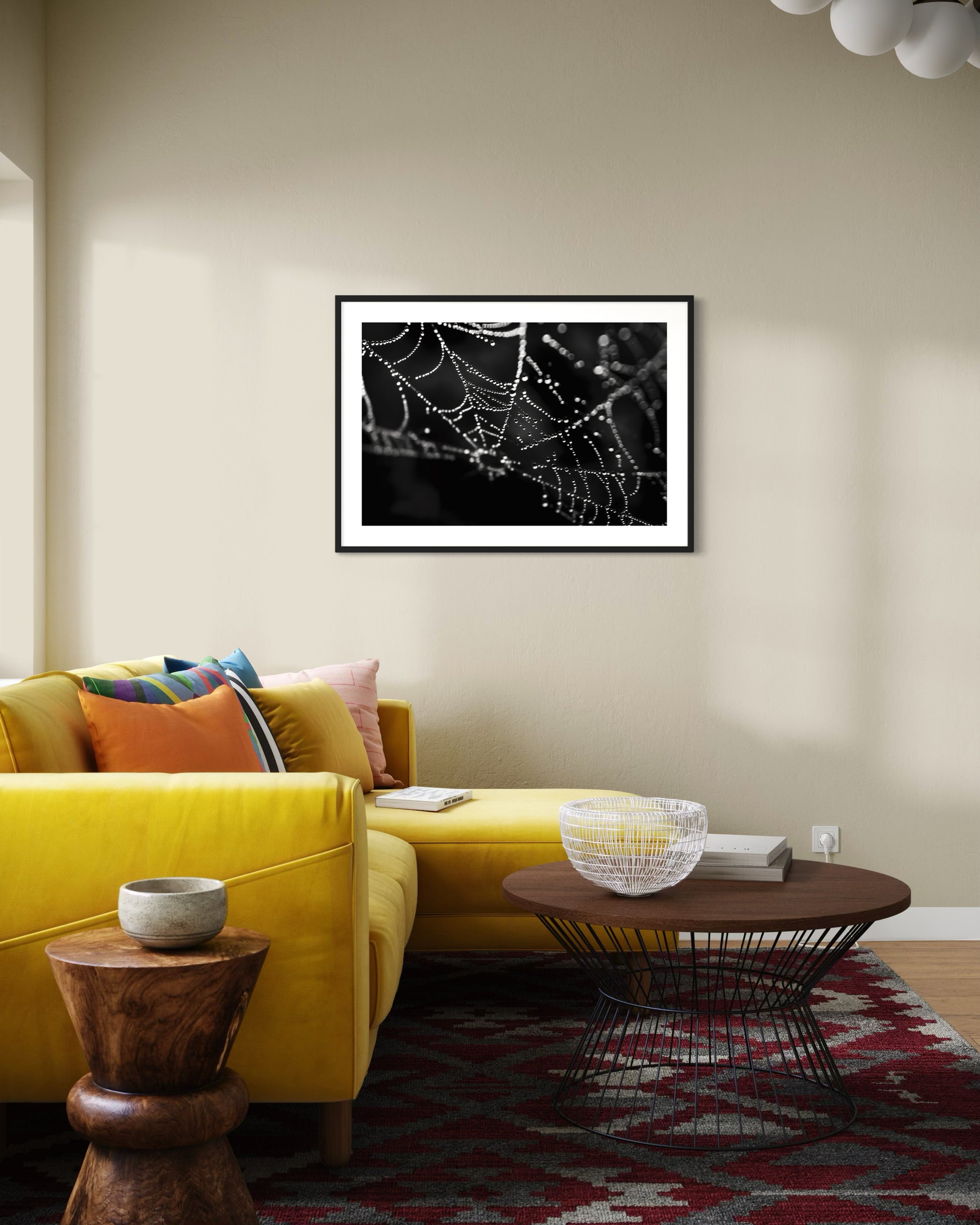 close up photo of rain drops on spider web in black and white in black frame with white matte on light tan wall in modern living room with bright yellow couch