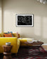 close up photo of rain drops on spider web in black and white in black frame with white matte on light tan wall in modern living room with bright yellow couch
