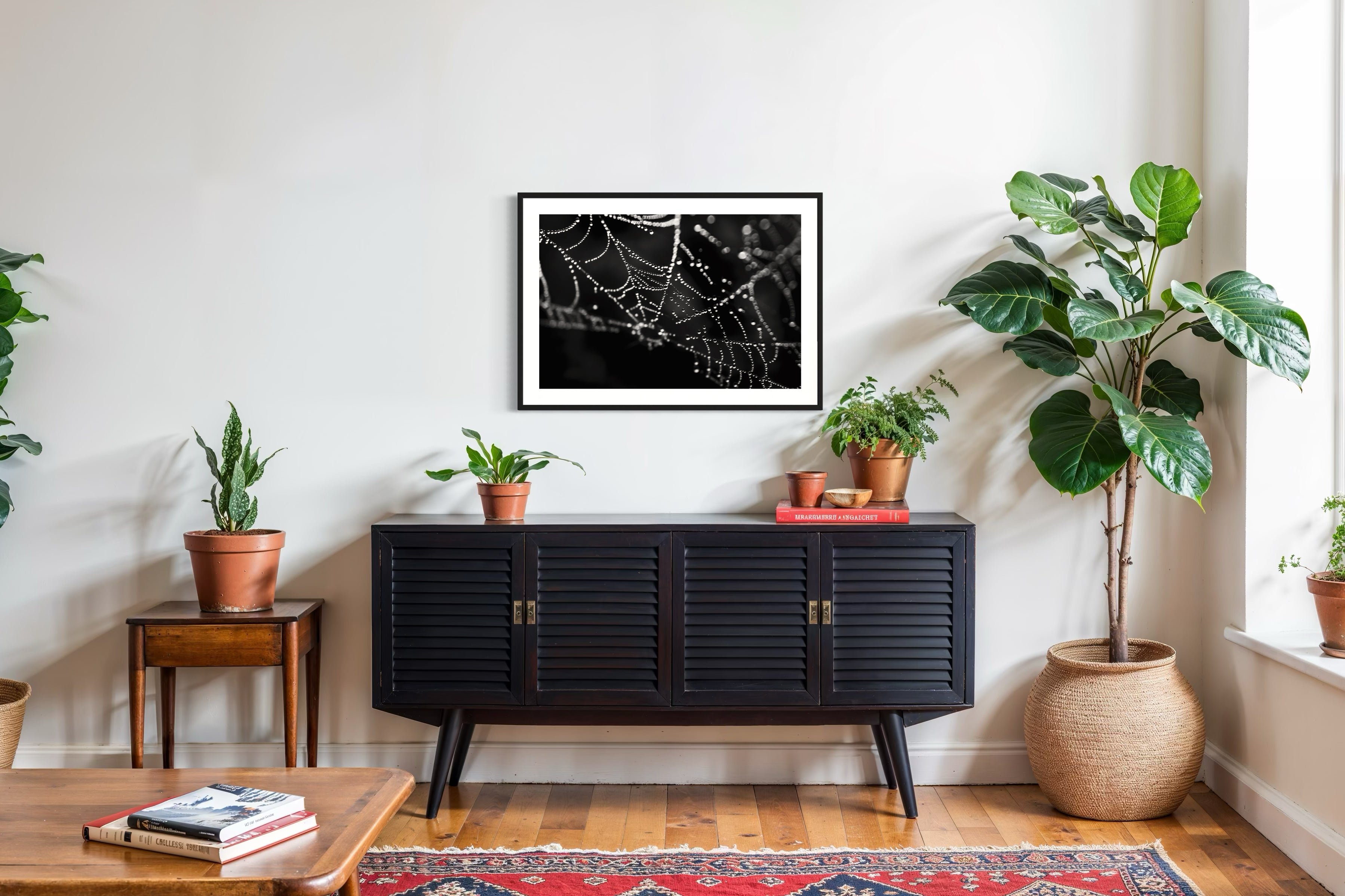 close up photo of rain drops on spider web in black and white in black frame with white matte on white wall above black piece of furniture 