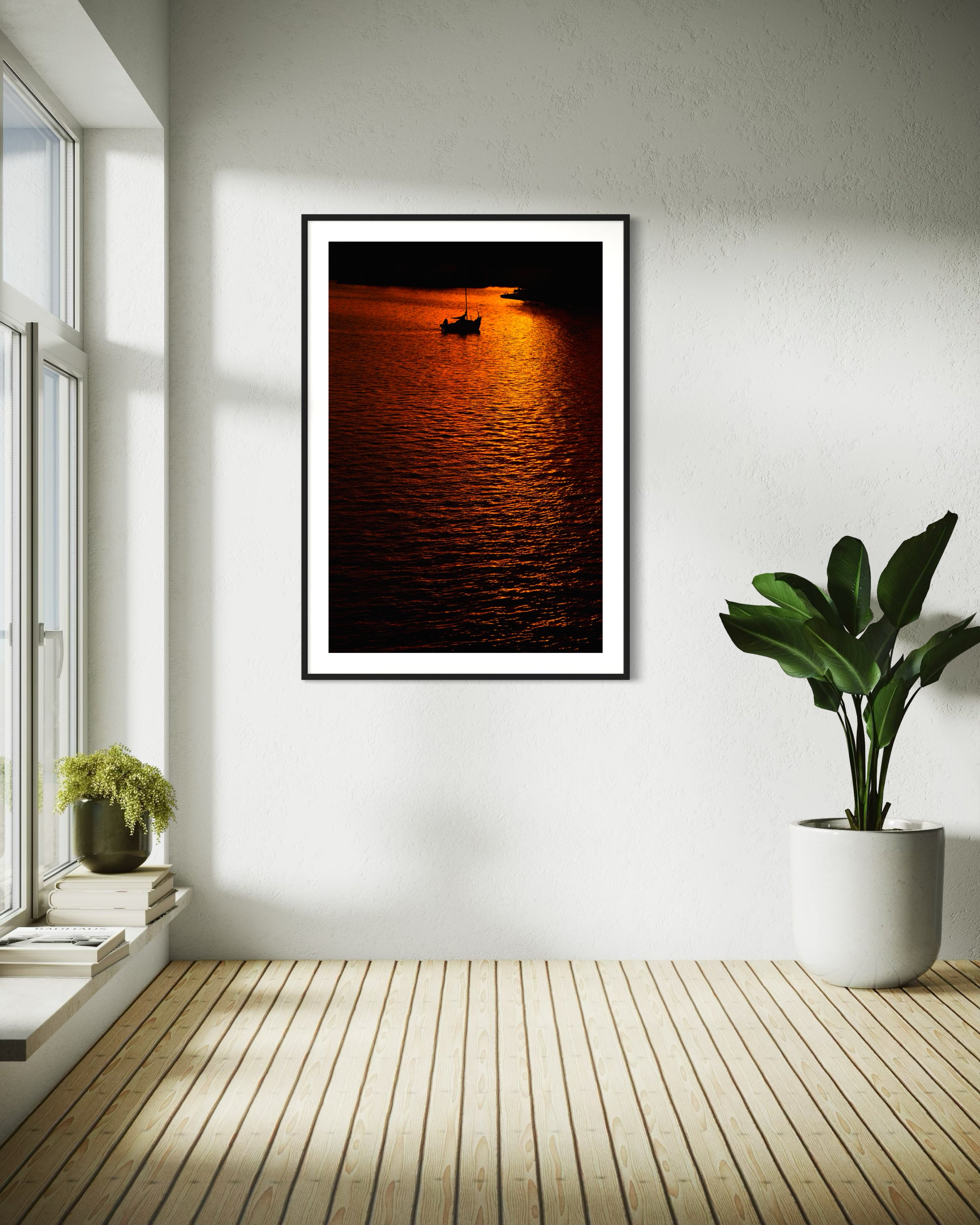 photo of sailboat sailing at sunset, in a very warm tone in black frame with white matte on white wall in corner of minimalist home