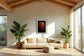 photo of sailboat sailing at sunset, in a very warm tone in black frame with white matte on white wall in Scandinavian style living room with tan couch, 2 tall green plants and exposed beams in the ceiling