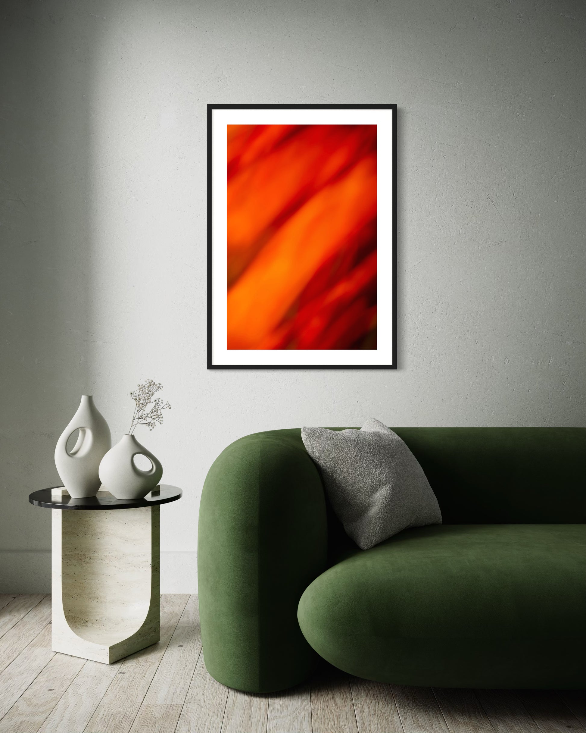 orange abstract with upward motion in black frame with white matte on light gray wall above dark green puffy modern couch with end table
