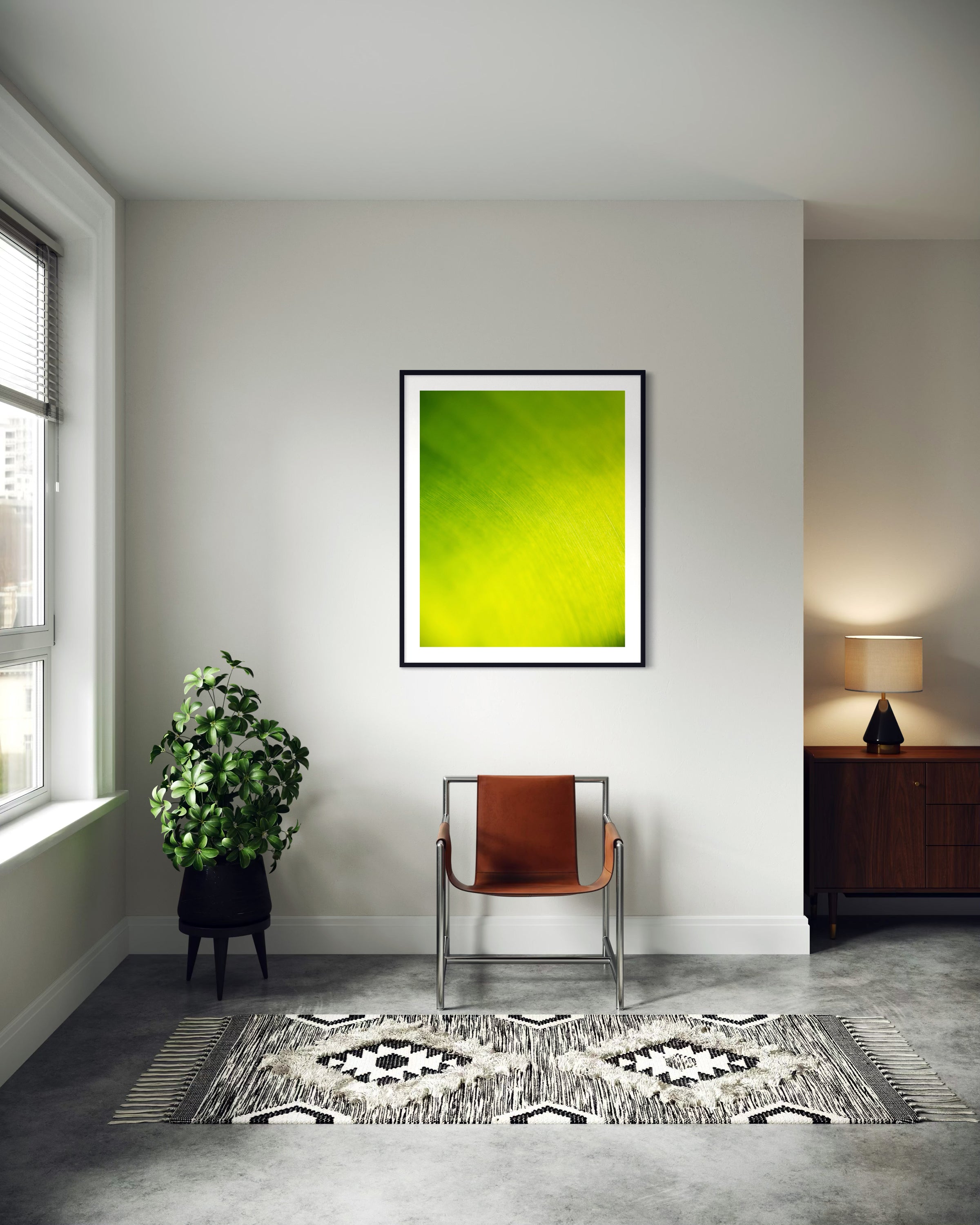 close up of large tropical leaf with the lines flowing like a waterfall in black frame with white matte on light gray wall in minimalist sitting area with concrete floors, one chair and one plant